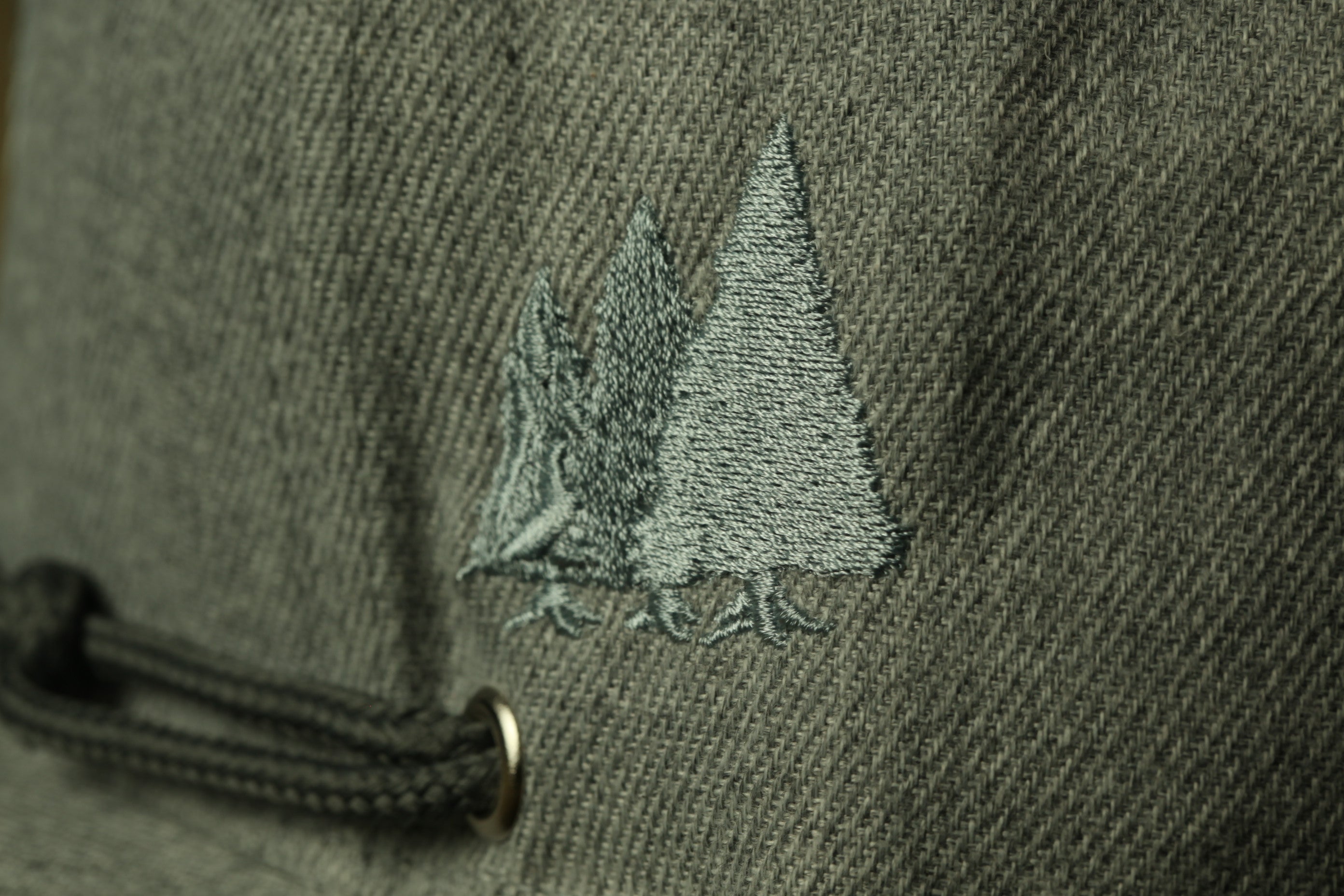 a close-up view of a gray fabric with a small embroidered design featuring two trees on the left side.