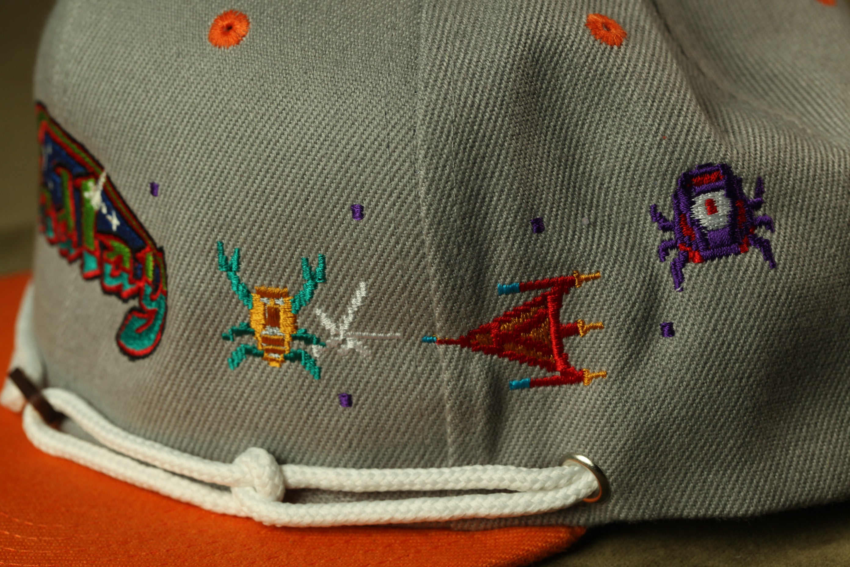 a gray baseball cap with colorful embroidered designs, including a crab, a flag, and other abstract shapes.