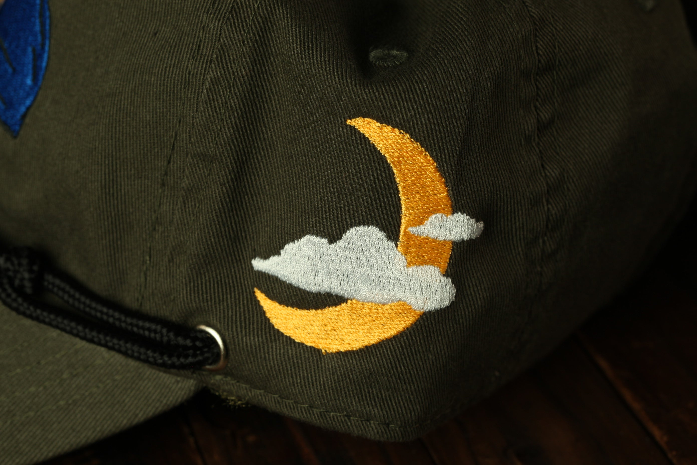 a close-up view of a dark green fabric with a yellow crescent moon and a white cloud embroidered on it.