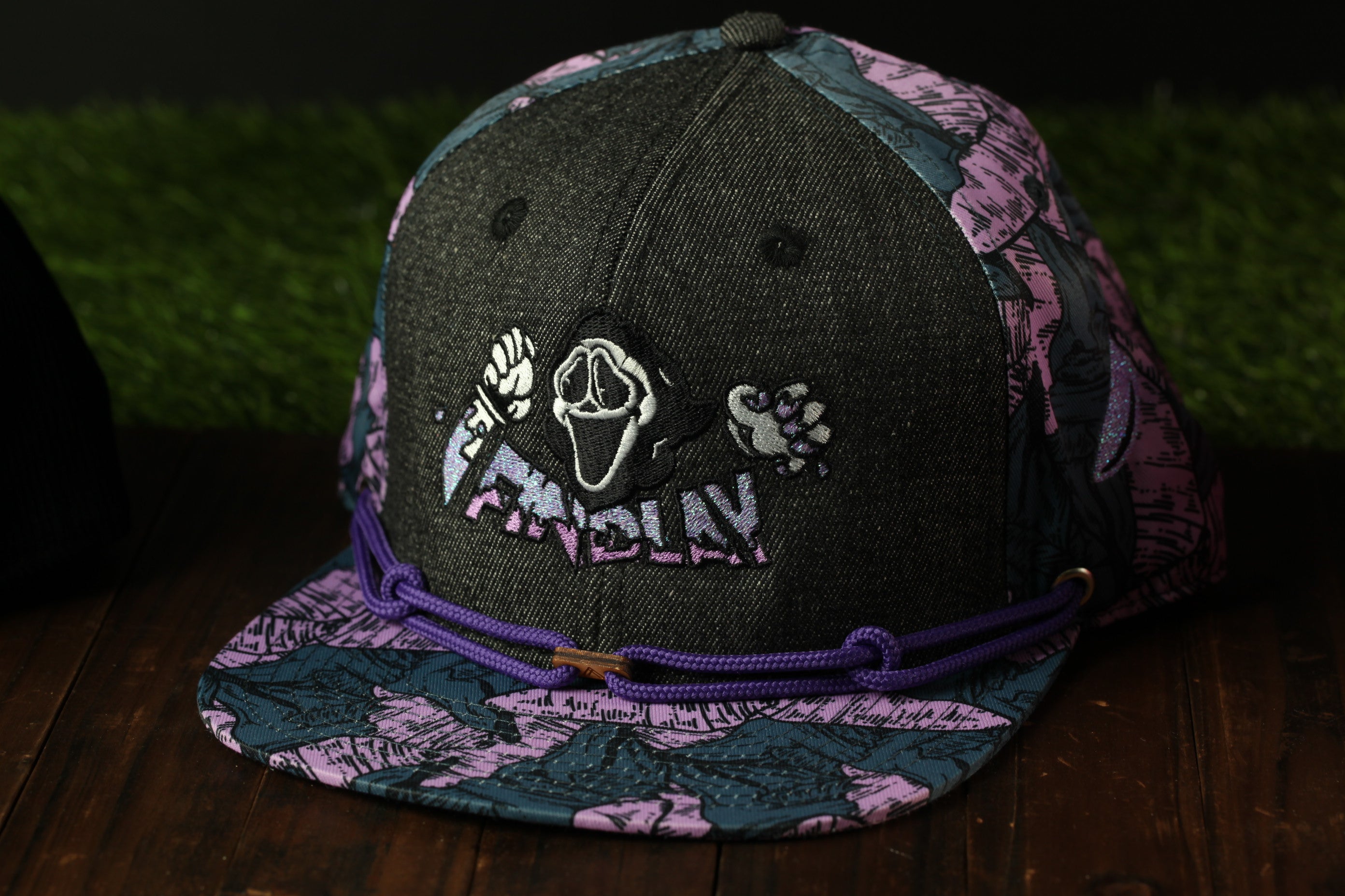 A black baseball cap with a purple and pink floral pattern, featuring a graphic of a ghost or skeleton on the front.