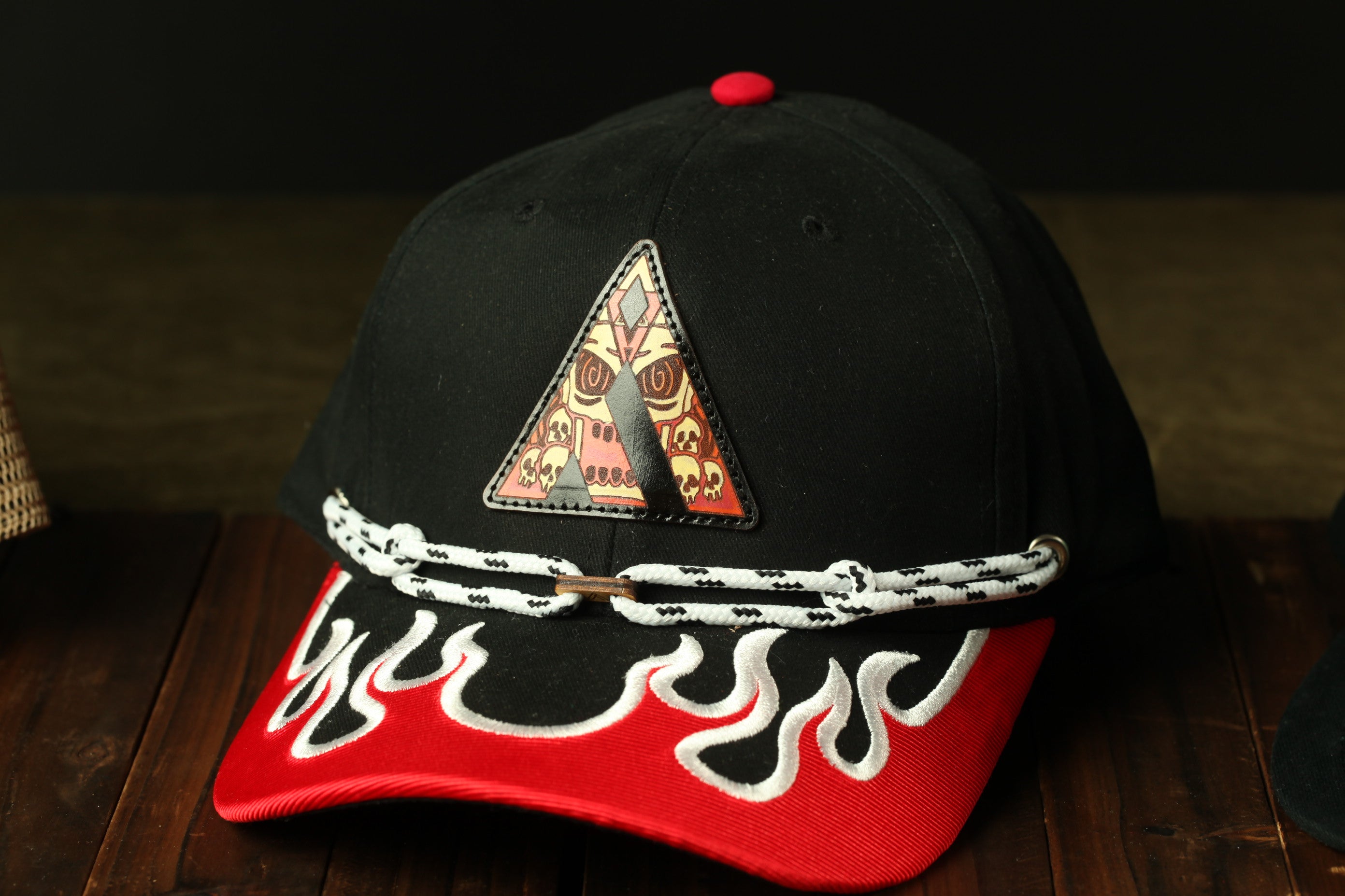 A black baseball cap with a red and white flame design on the front, sitting on a wooden surface.