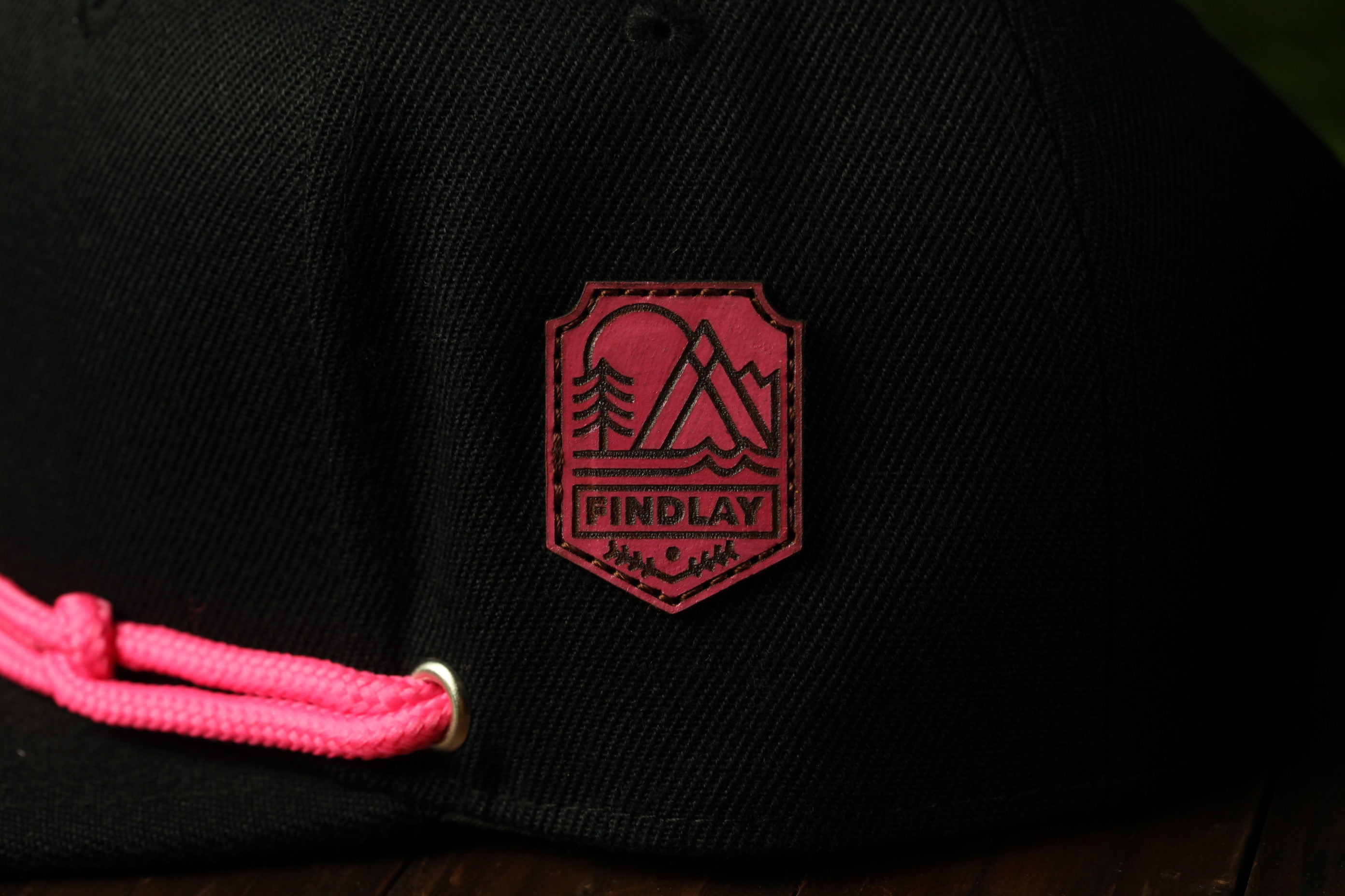 A close-up view of a black baseball cap with a red patch on the front, featuring a mountain and tree design.