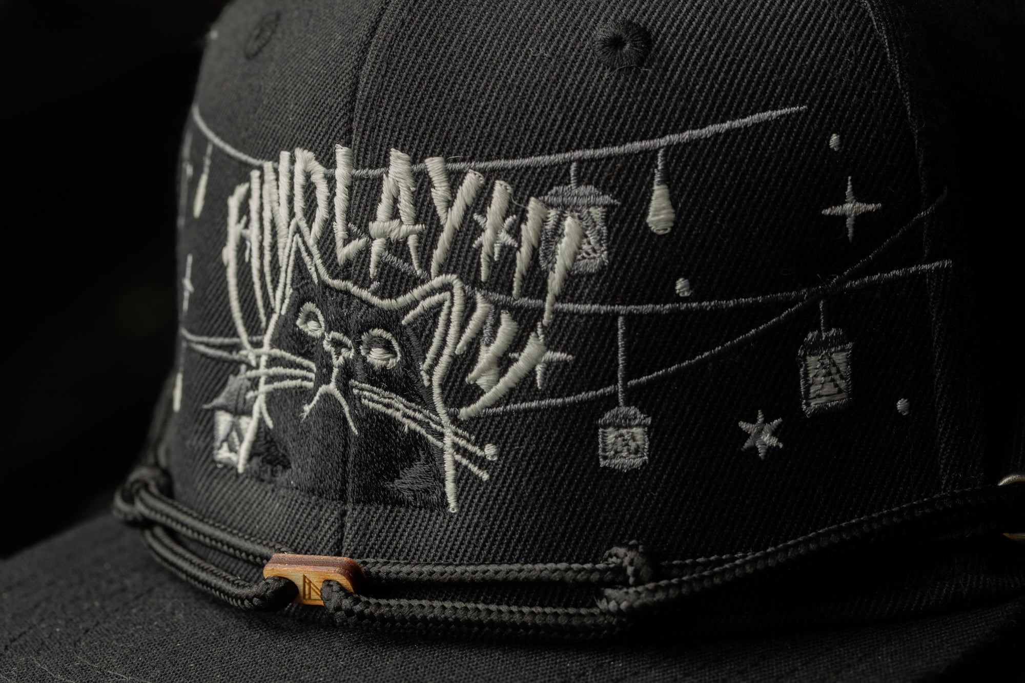 A close-up view of a black baseball cap with a unique embroidered design featuring a cat and various decorative elements.