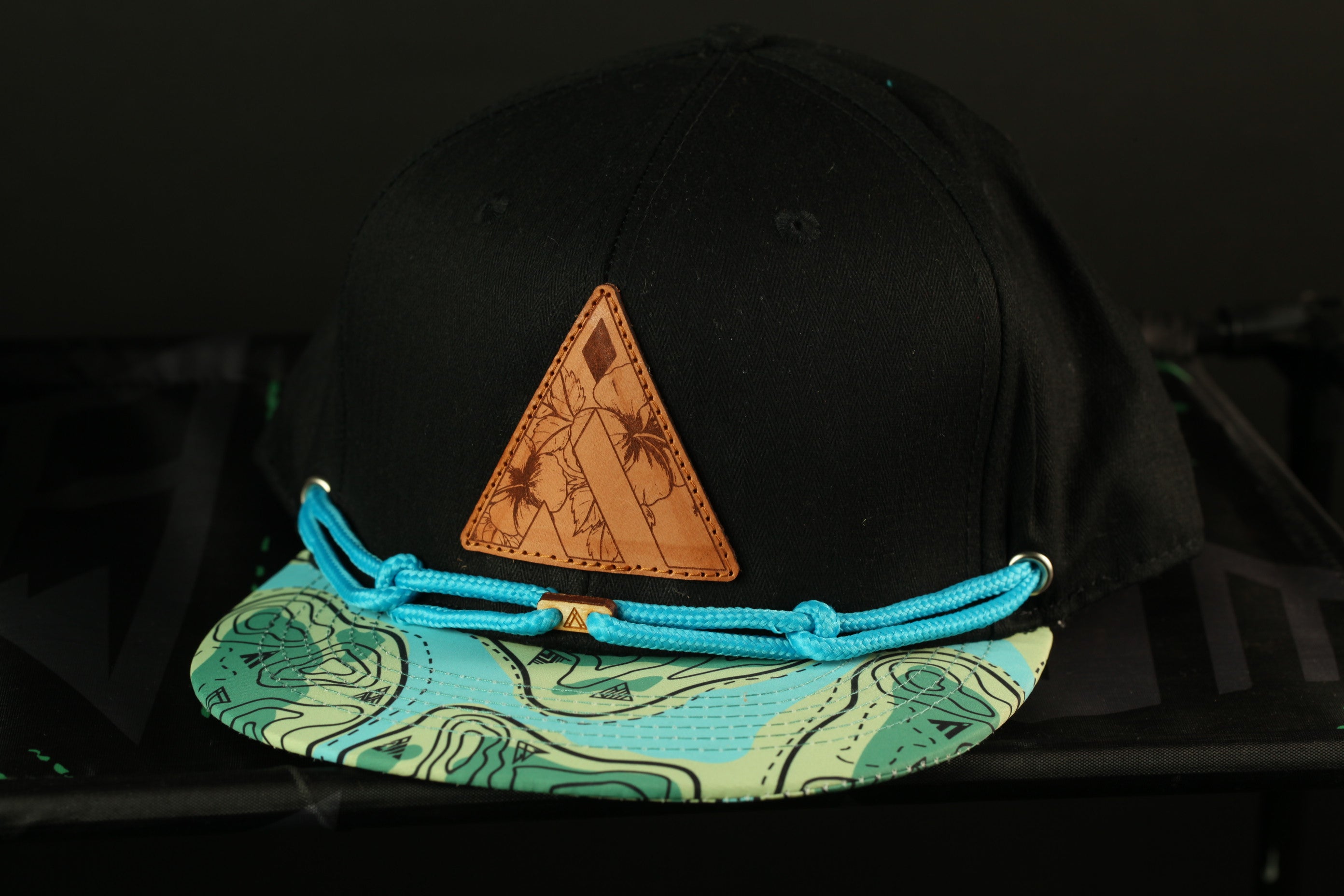 A black baseball cap with a leather patch and a blue string around the brim.