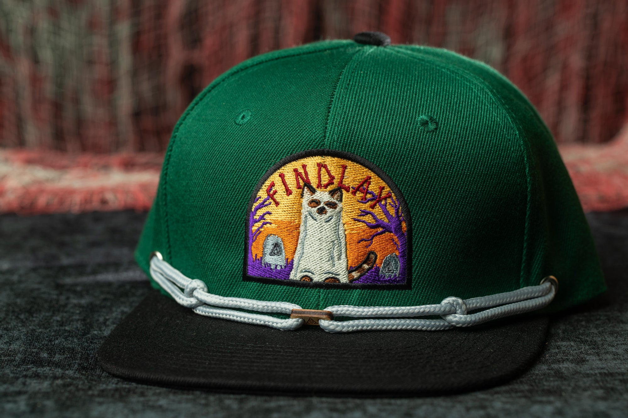 A green baseball cap with a colorful embroidered patch on the front, featuring a cat and the text "FINDA".