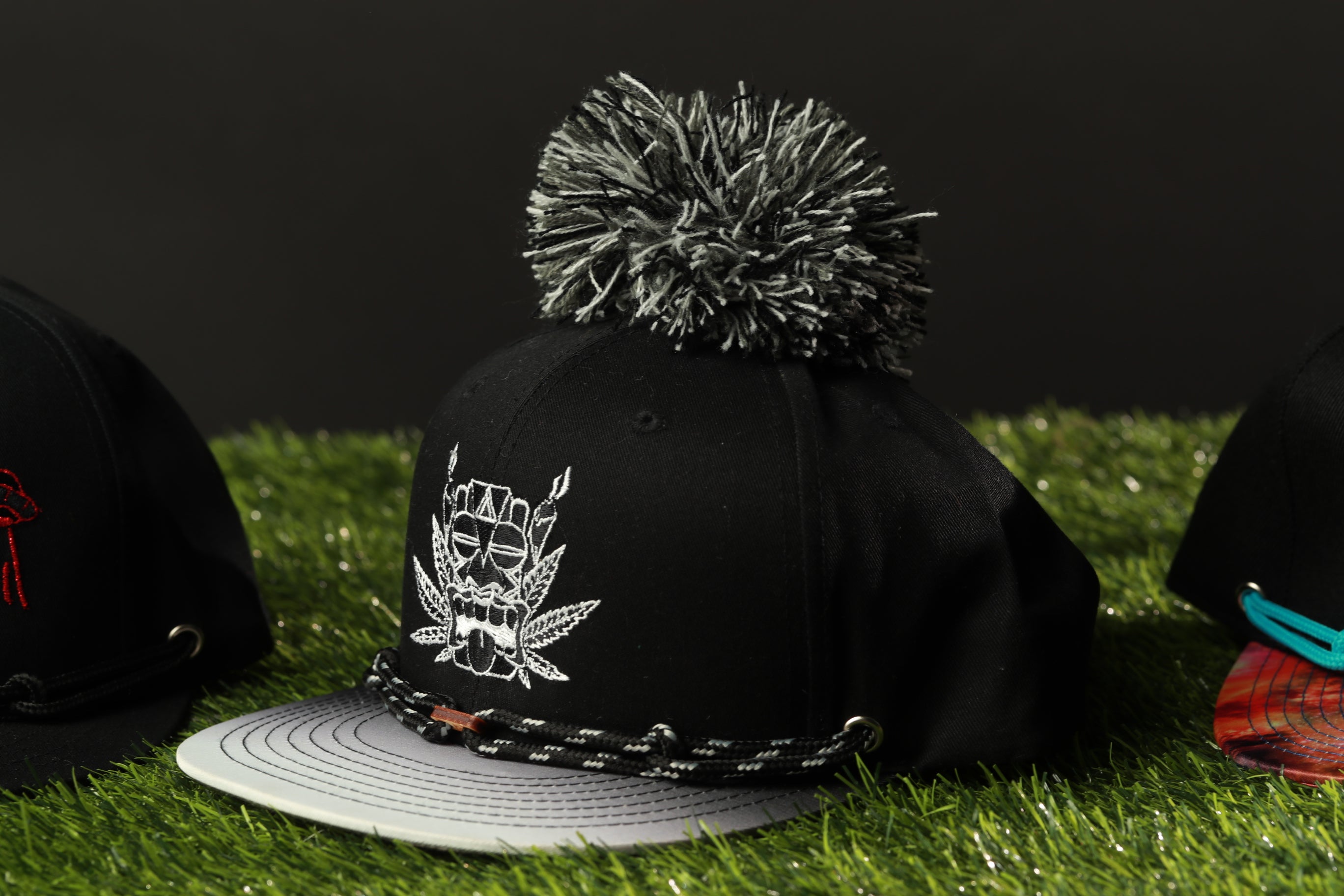 A close-up view of a black baseball cap with a pom pom on top, placed on a grassy surface.