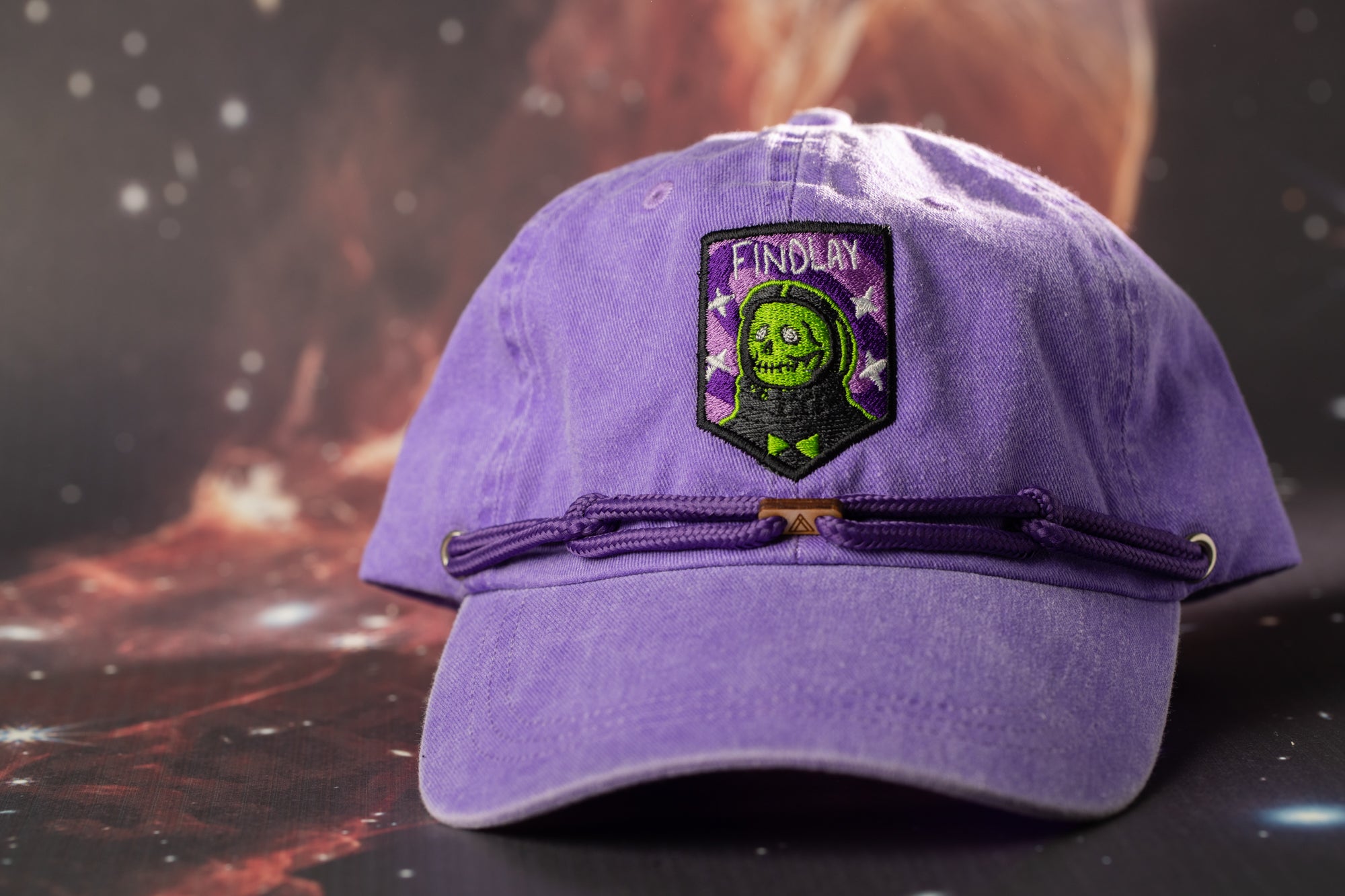 A purple baseball cap with a purple and green skull design and the word "FINDLAY" on the front.