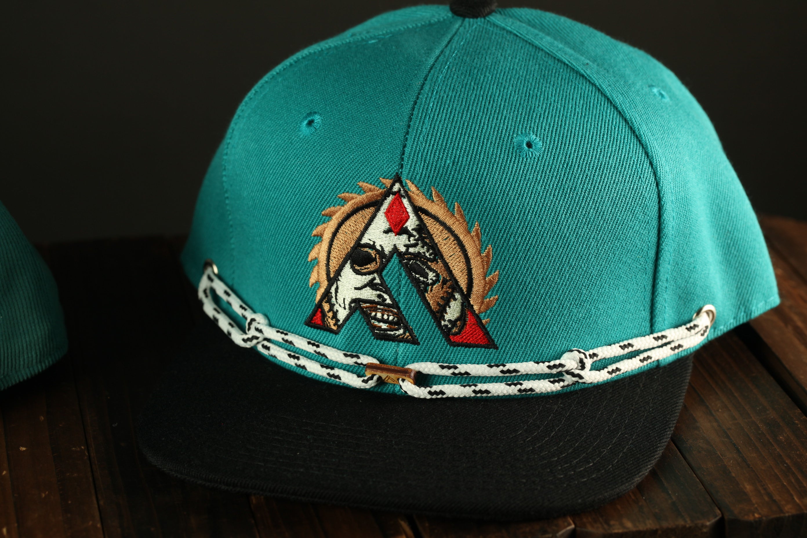 A turquoise baseball cap with a black brim and a white and black chain strap.