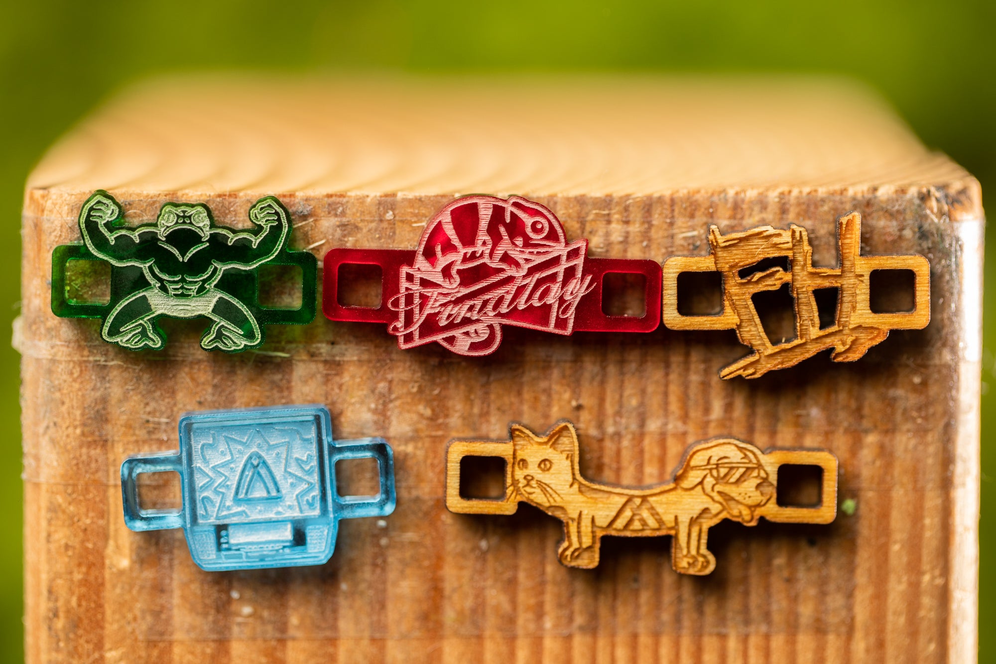 a collection of colorful, hand-crafted wooden charms or badges, each with unique designs and shapes, attached to a wooden surface.