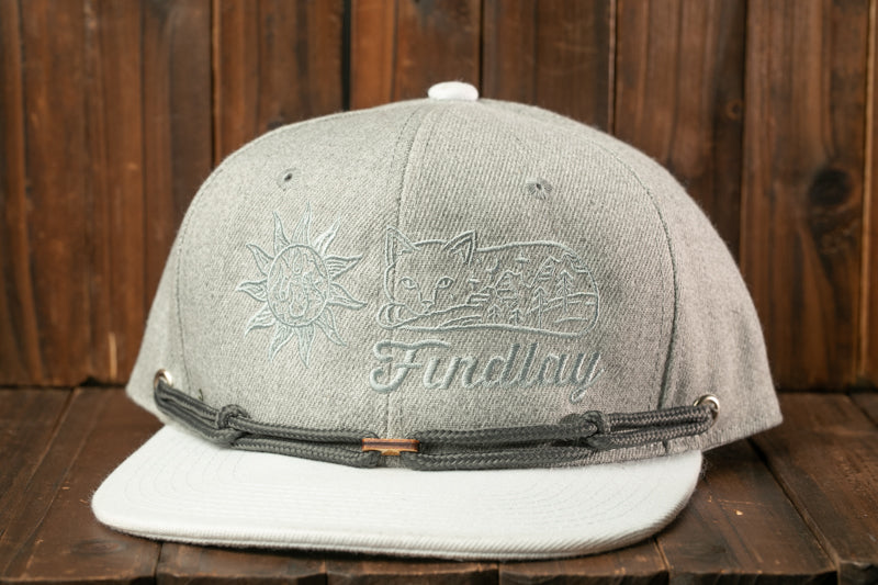 A gray baseball cap with a white brim and a black strap, featuring a sun design and the word "Findlay" printed on it.