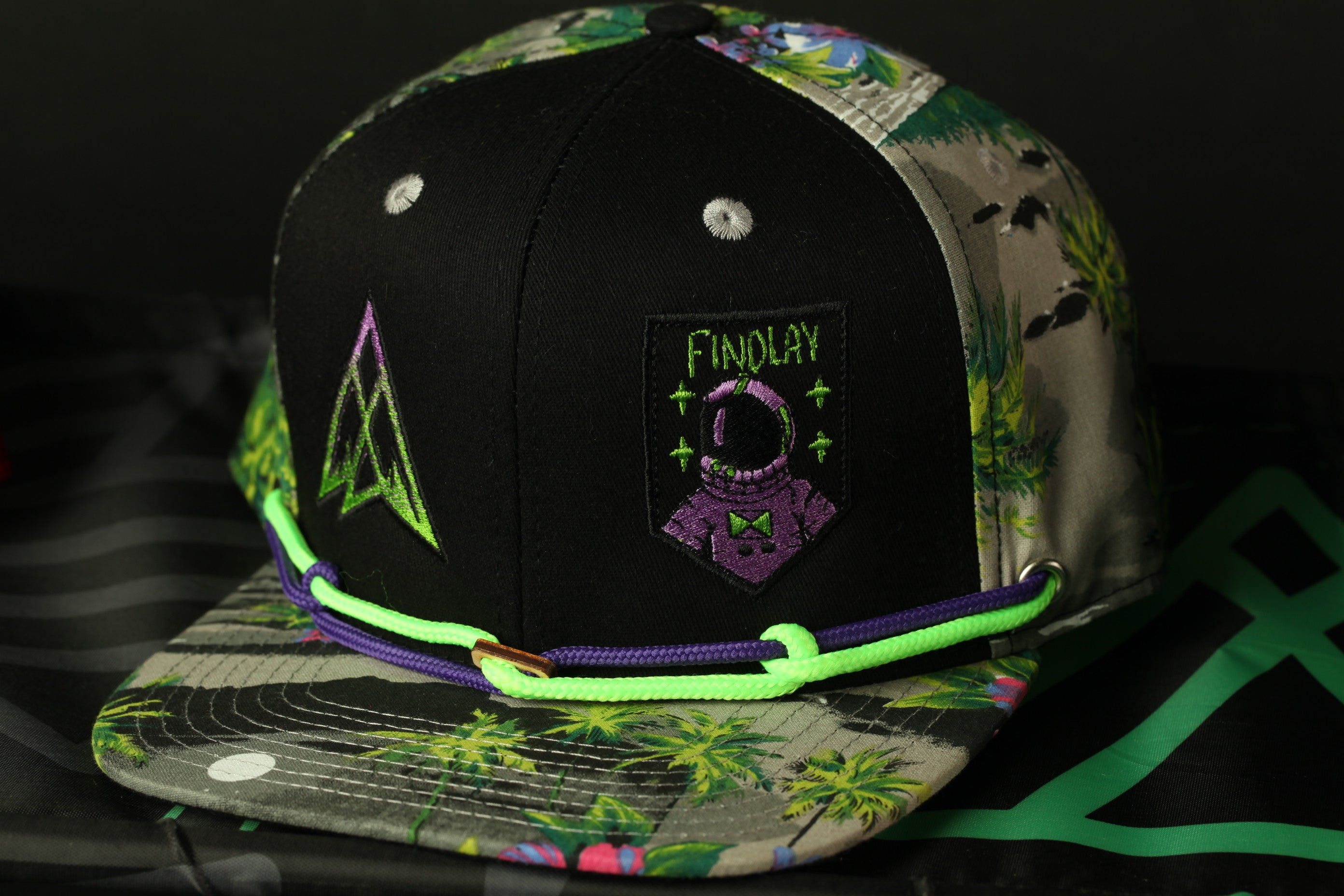 A colorful baseball cap with a floral pattern and a patch featuring a purple alien character.