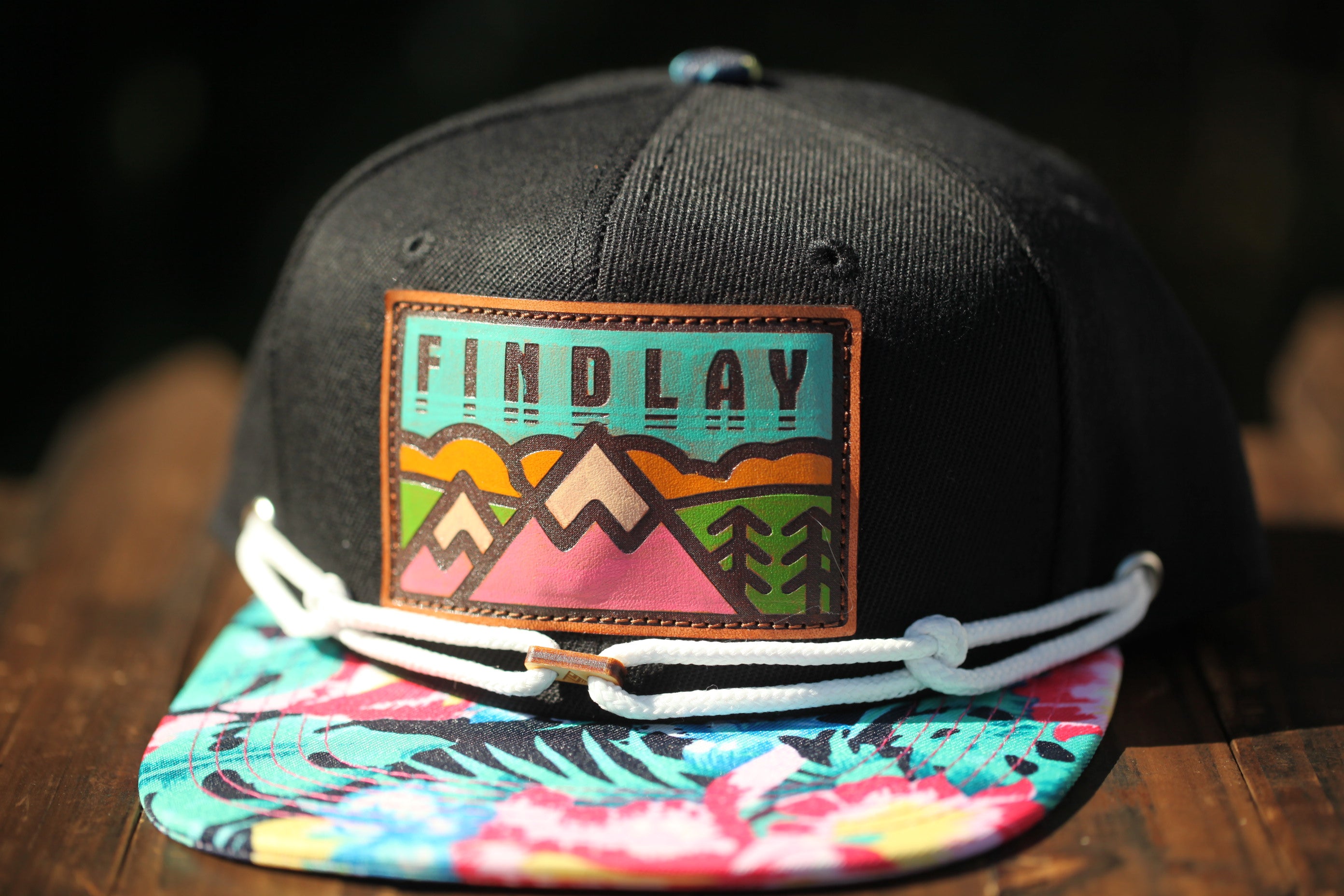 A black baseball cap with a colorful floral pattern and a patch that says "FIND LAY" on it.