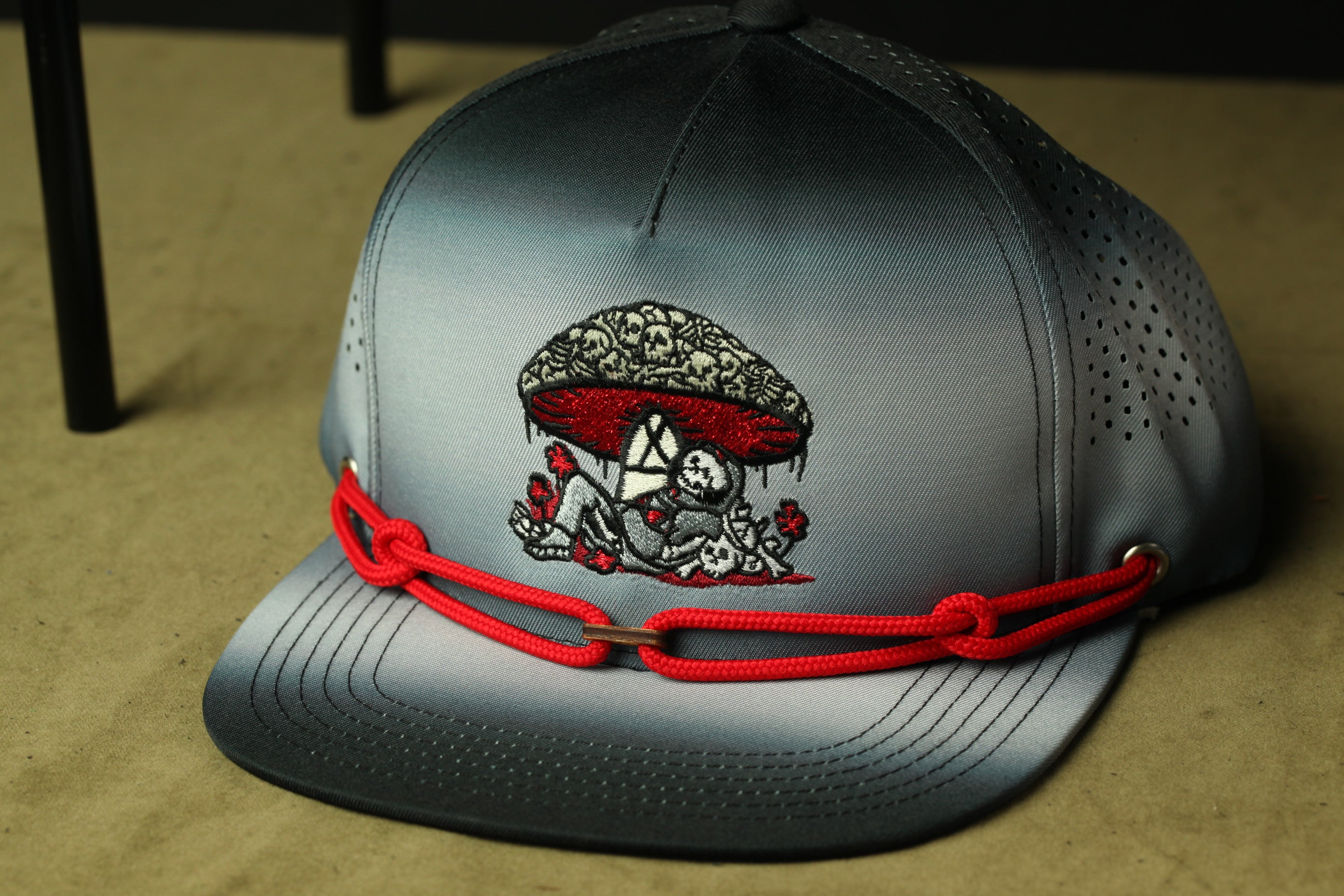 A gray baseball cap with a red rope and a mushroom design on the front.