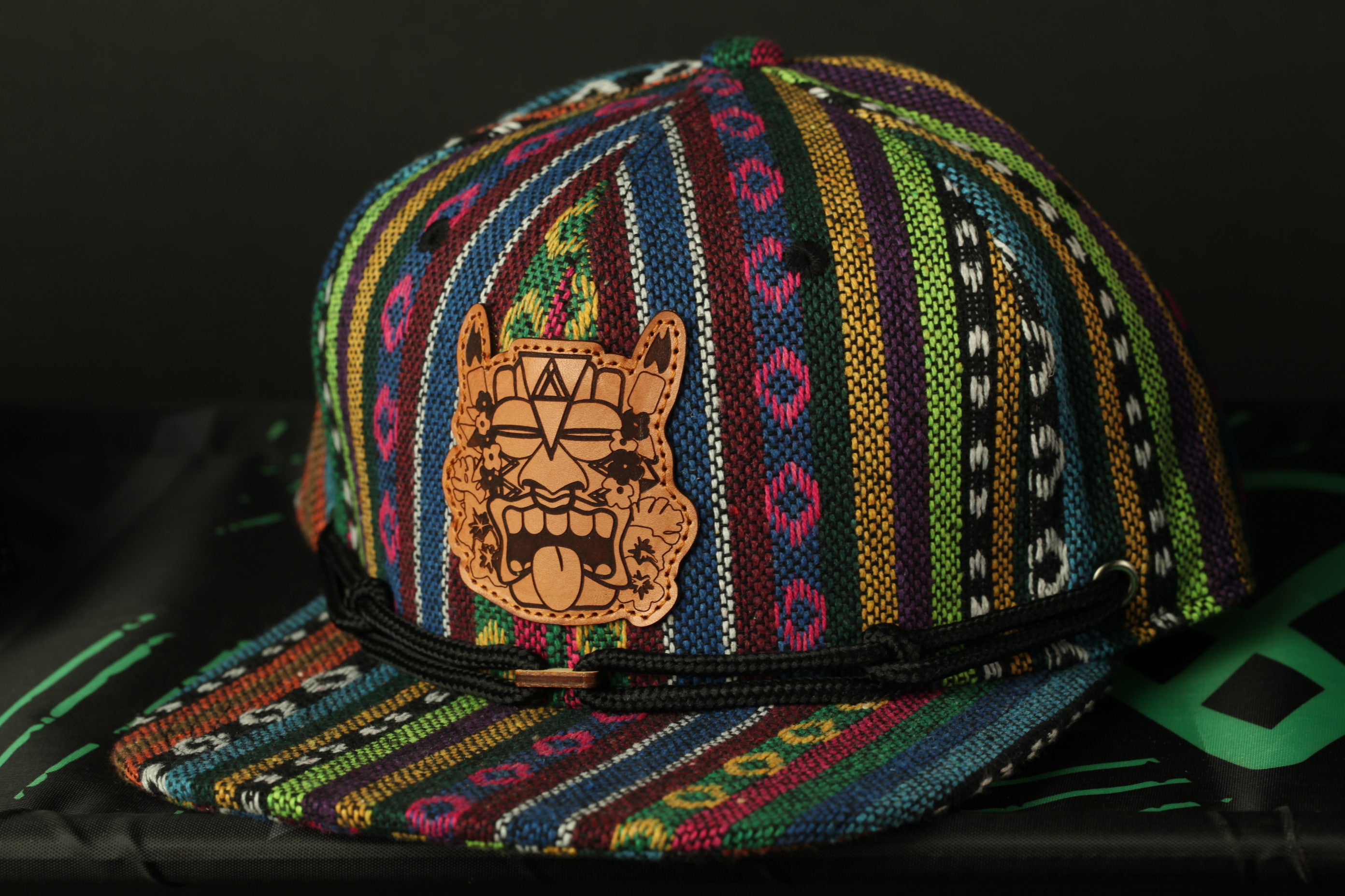 A colorful, patterned baseball cap with a leather patch featuring a stylized face design.