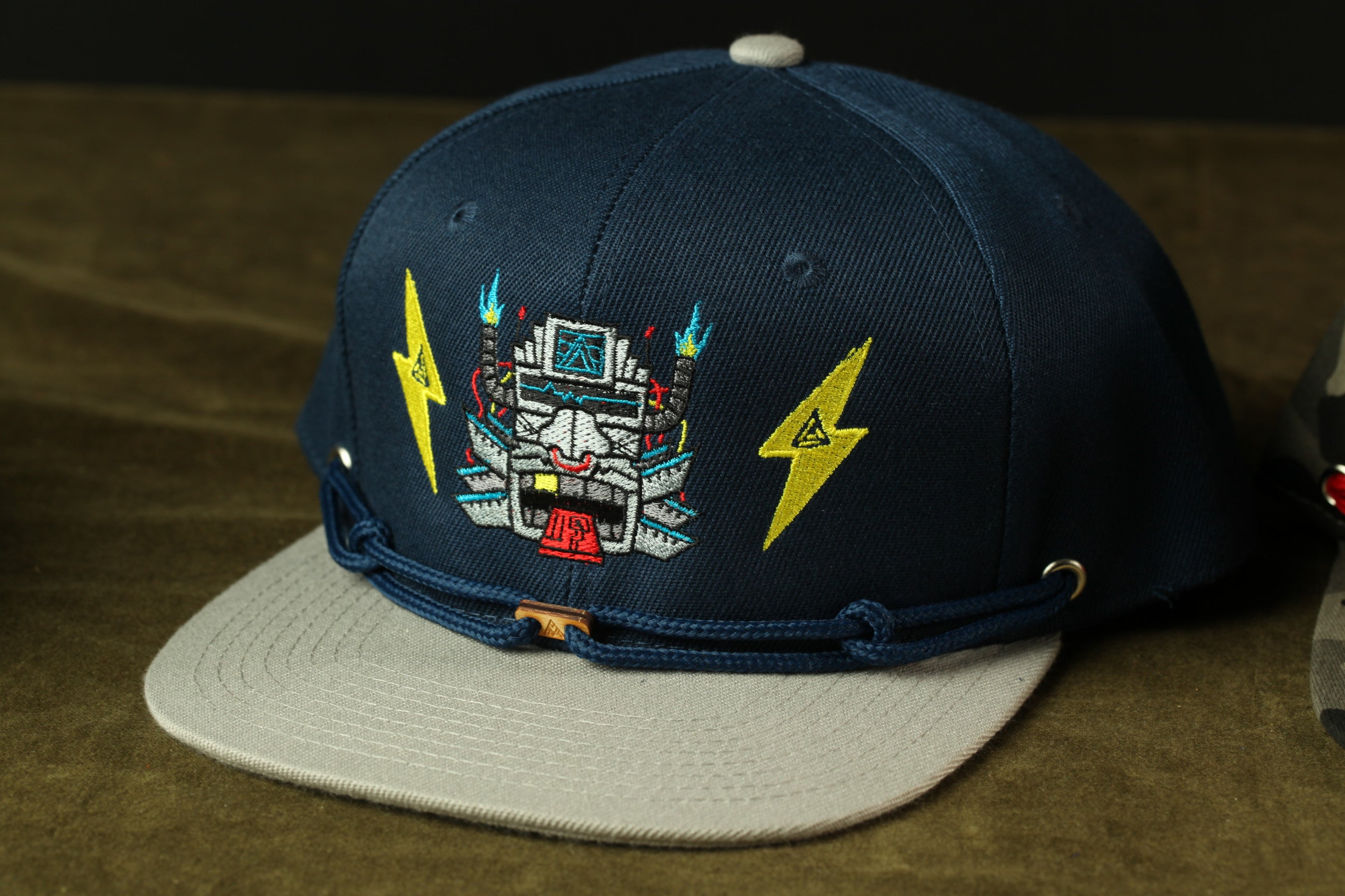 A navy blue baseball cap with a graphic design on the front, featuring a robot or mechanical figure with a lightning bolt symbol.