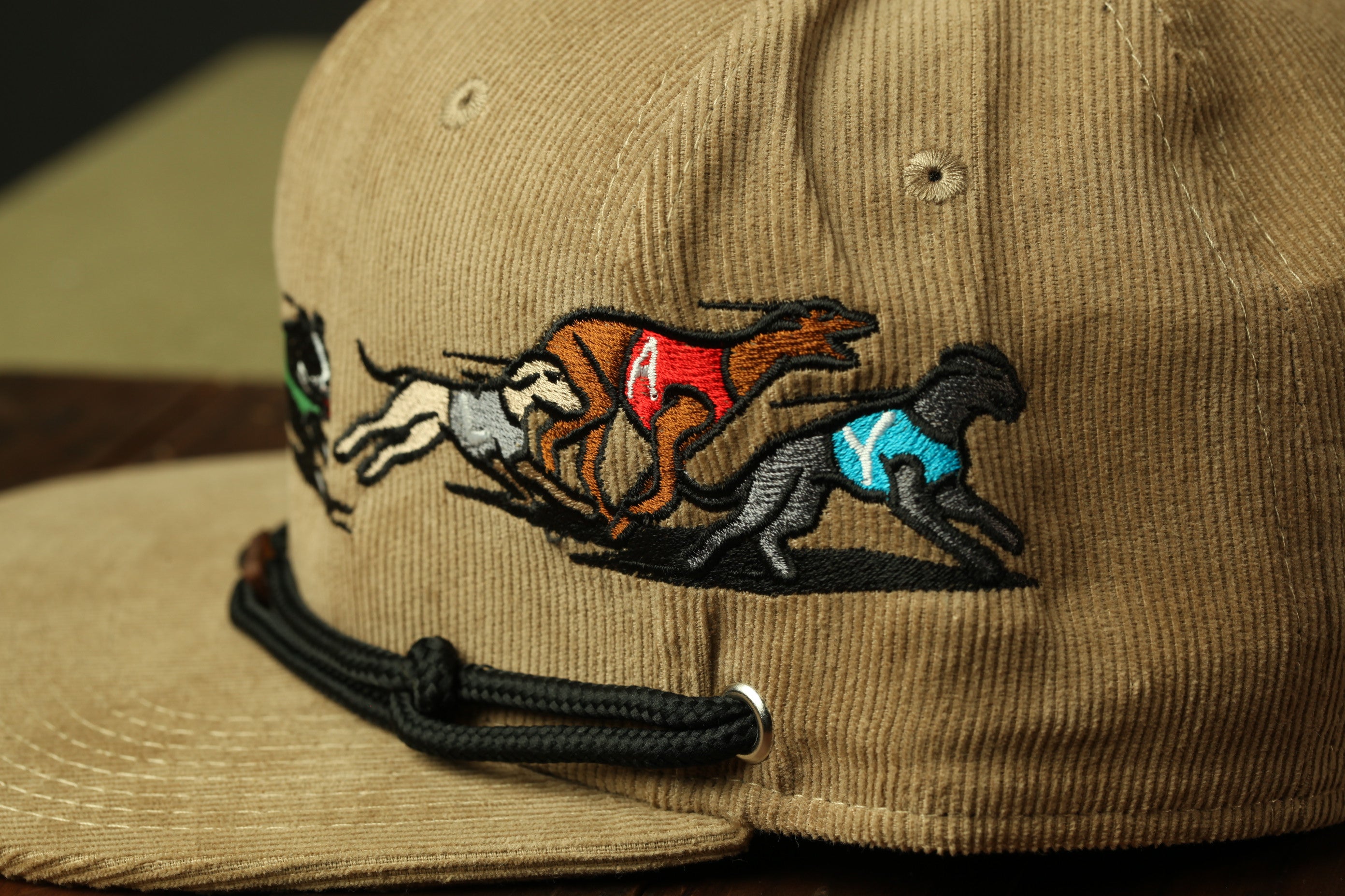A close-up view of a beige baseball cap with a detailed embroidered design depicting a group of dogs running together.