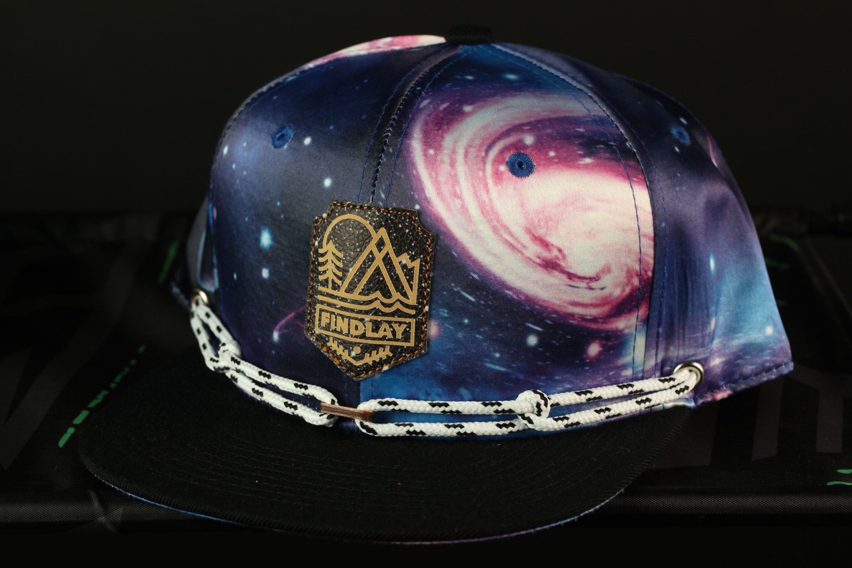 A colorful baseball cap with a space-themed design, featuring a galaxy pattern and a mountain-like logo.