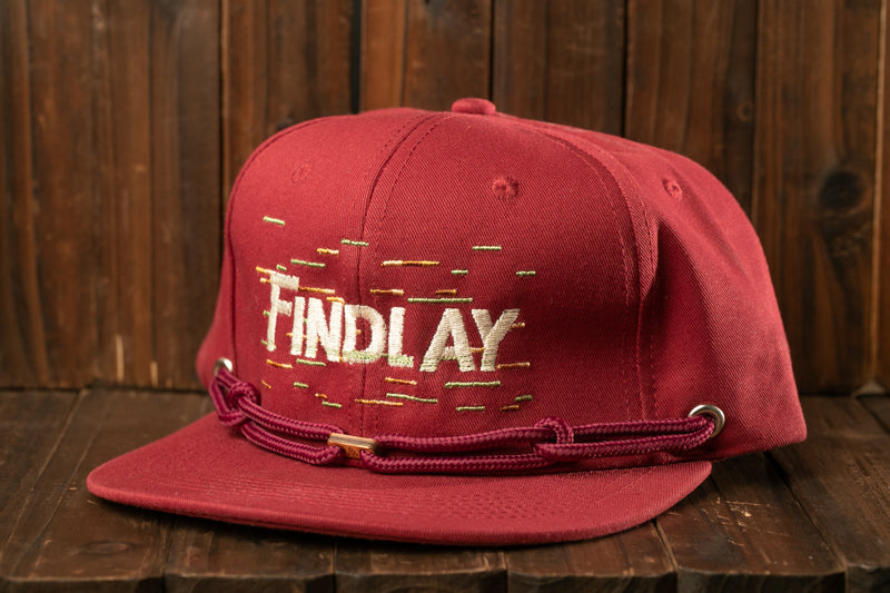 A red baseball cap with the word "Findlay" embroidered on it, sitting on a wooden surface.