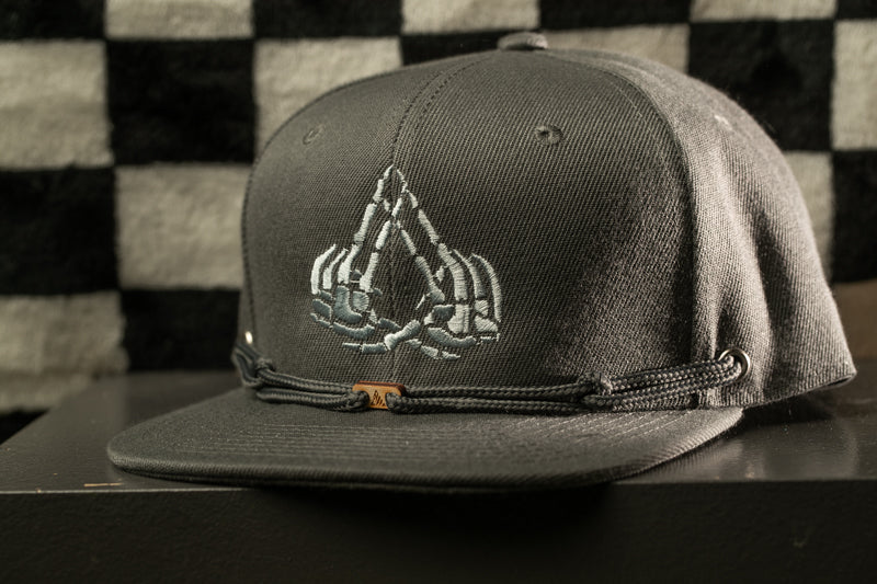A gray baseball cap with a unique skull-like design on the front, displayed against a black and white checkered background.