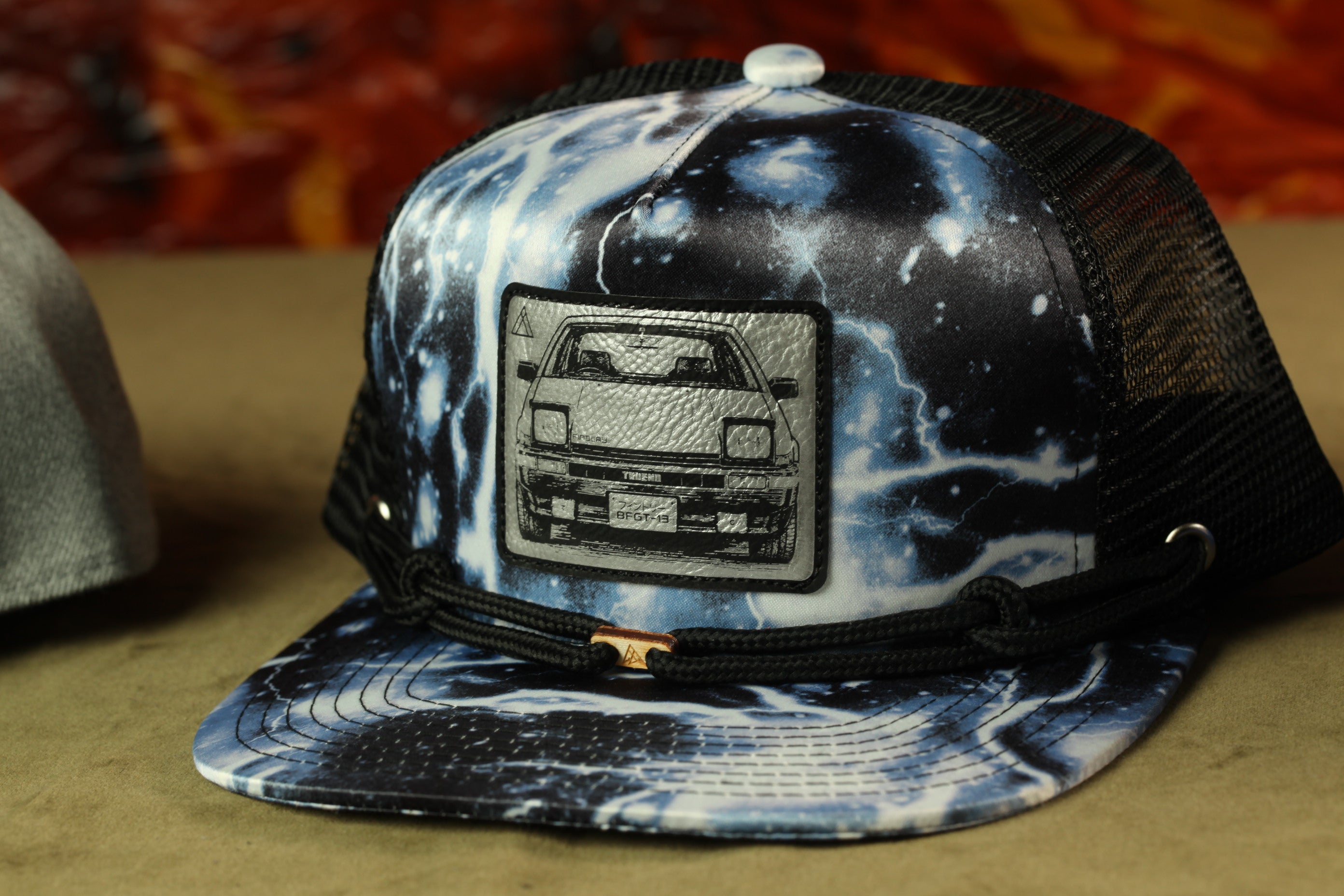 A black and white baseball cap with a printed design of a car on the front.