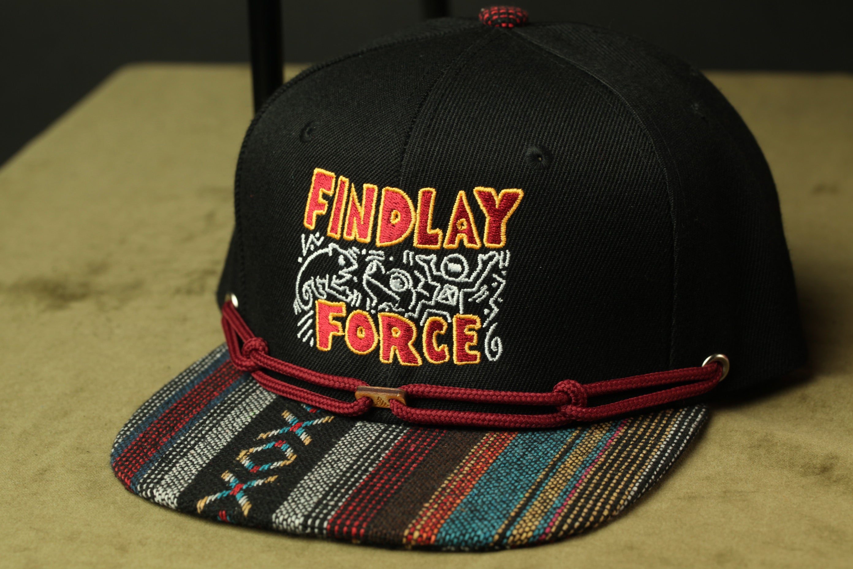 A black baseball cap with a colorful, patterned brim and a red string.