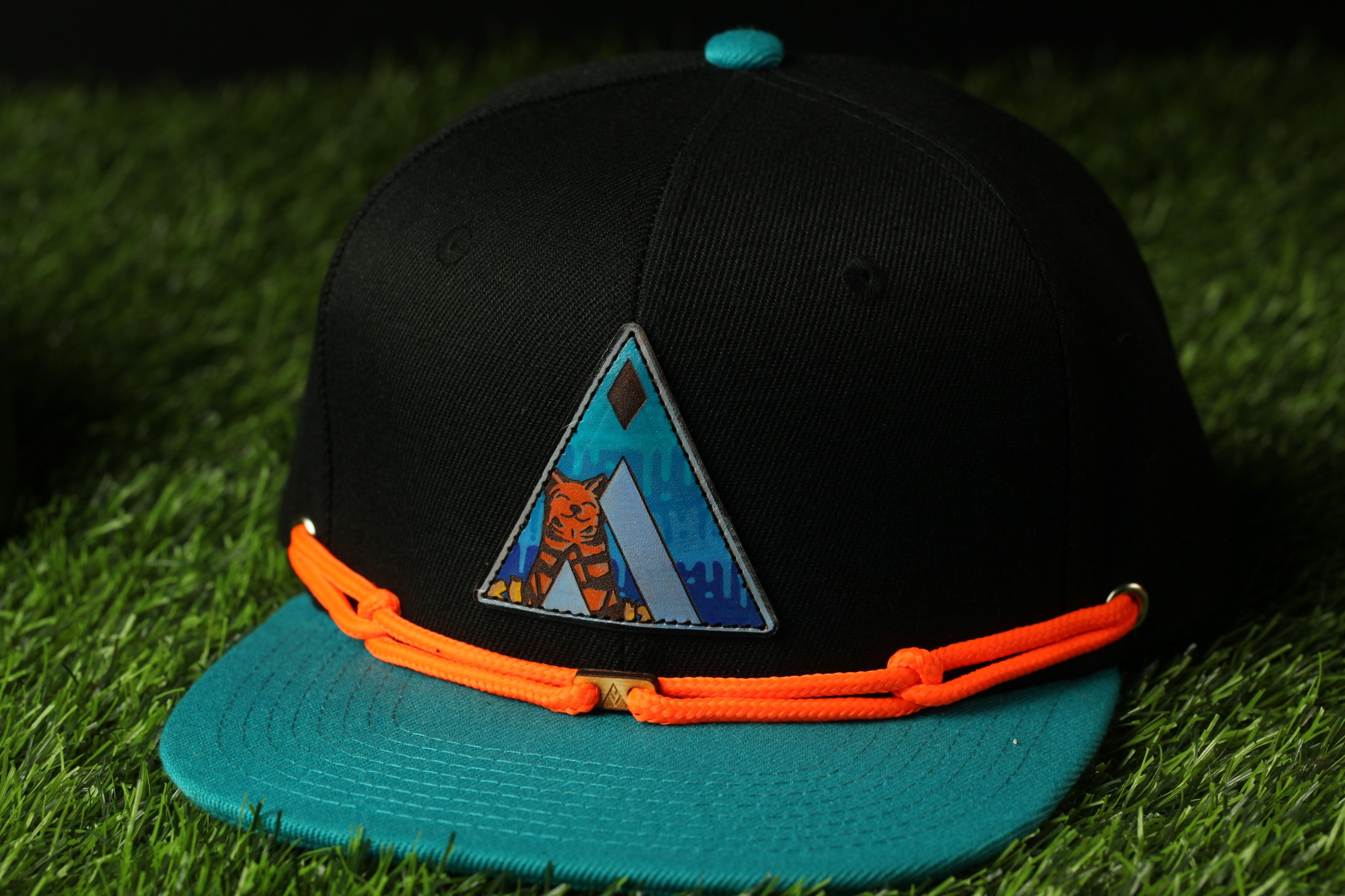 A black baseball cap with a blue and orange design on the front, placed on a grassy surface.