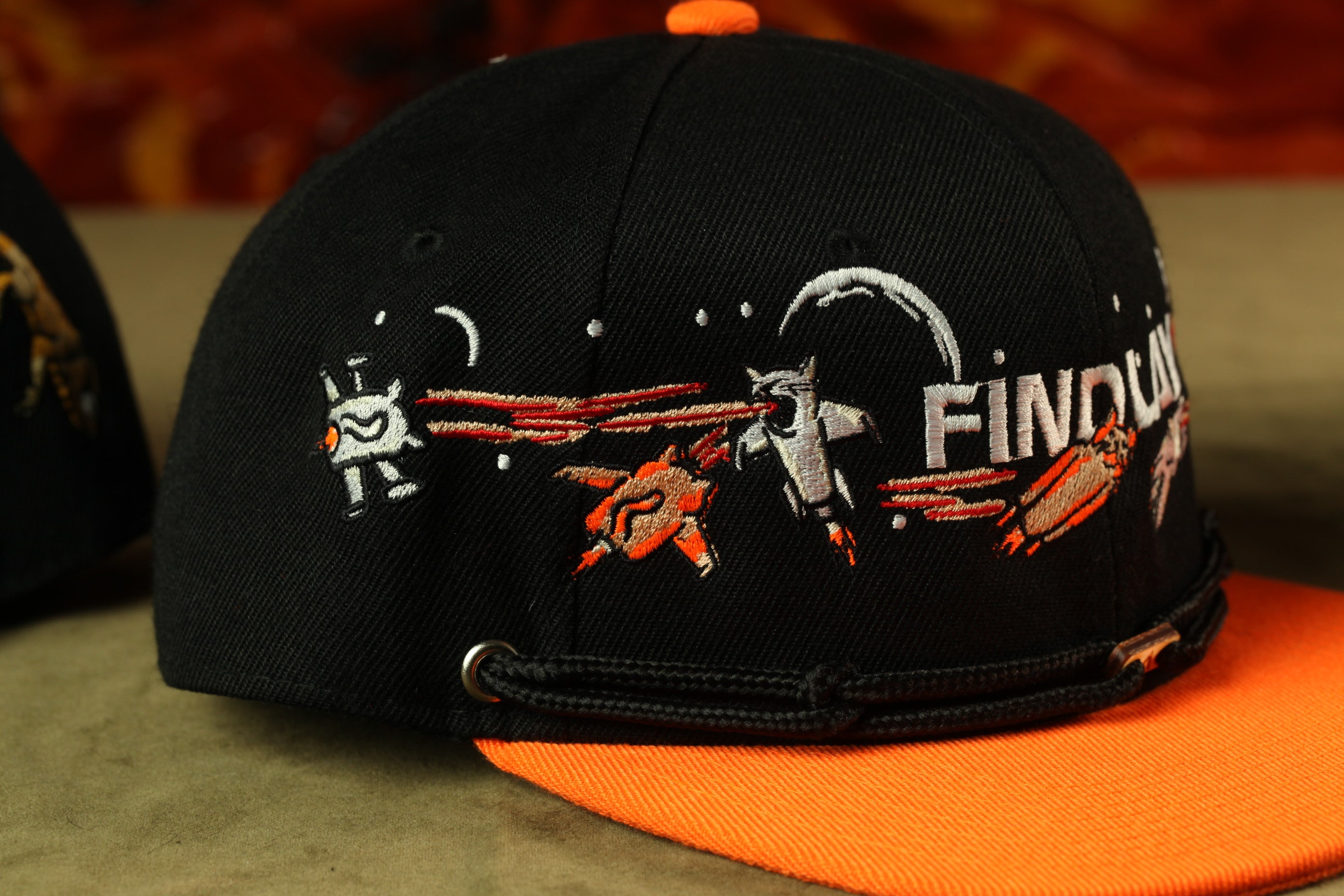 A black baseball cap with an orange brim, featuring a graphic design of a robot and a spacecraft.