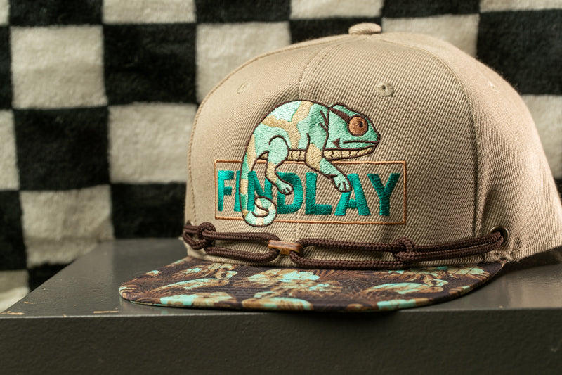A beige baseball cap with a graphic of a chameleon and the word "FINDA" printed on it.