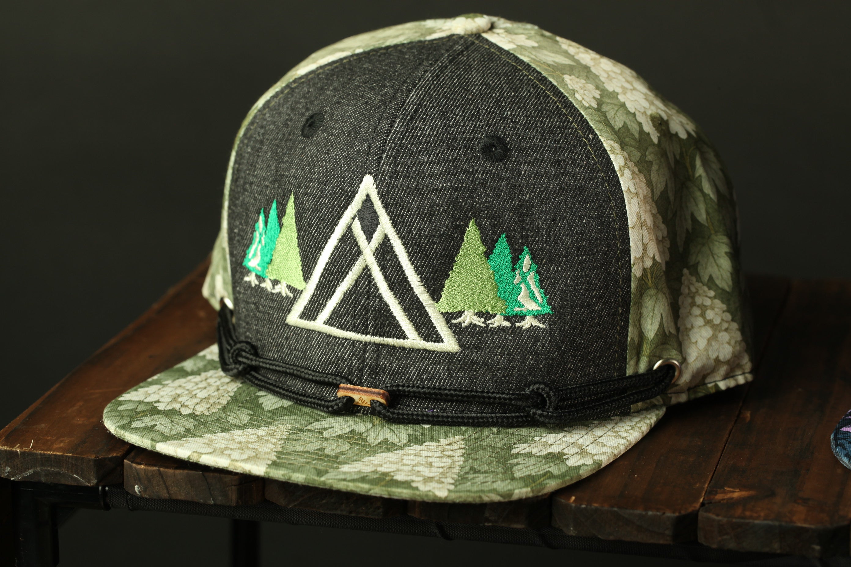 A black and green baseball cap with a floral pattern and a triangle design on the front, sitting on a wooden surface.