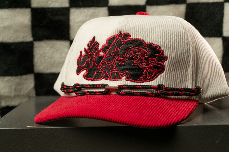 A white baseball cap with a red brim and a black and red embroidered logo on the front, sitting on a black surface against a black and white checkered background.