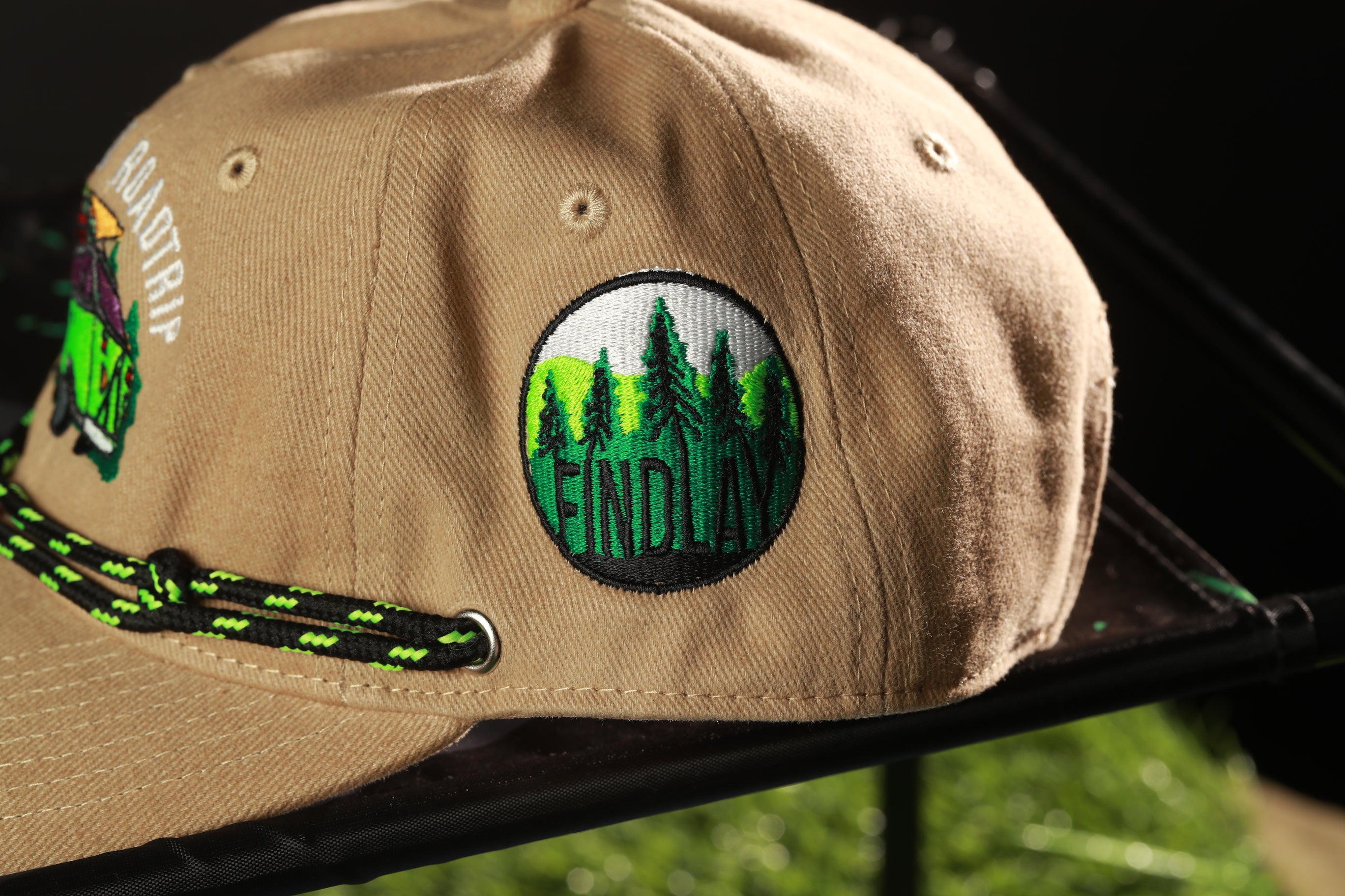 A tan baseball cap with a green and black lanyard, featuring a circular patch with the word "FINDLAY" printed on it.