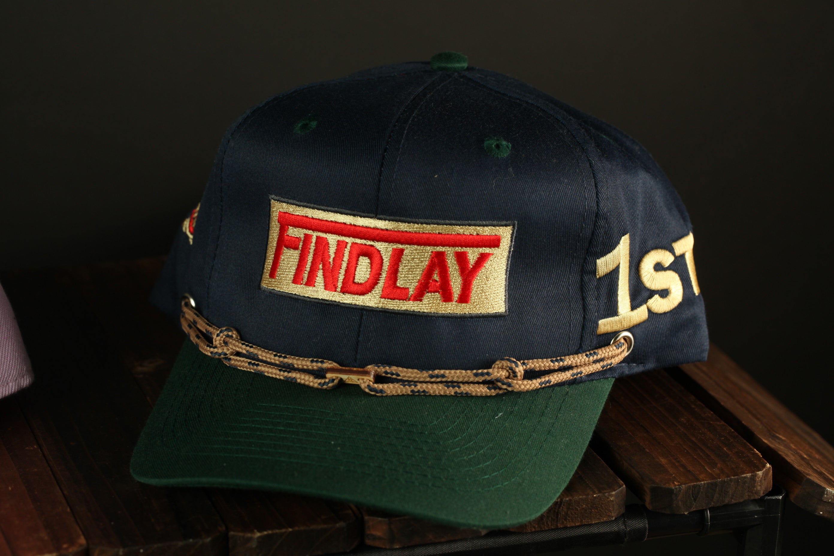 A navy blue baseball cap with a green brim and a red and gold patch that says "FINDlay" on it.