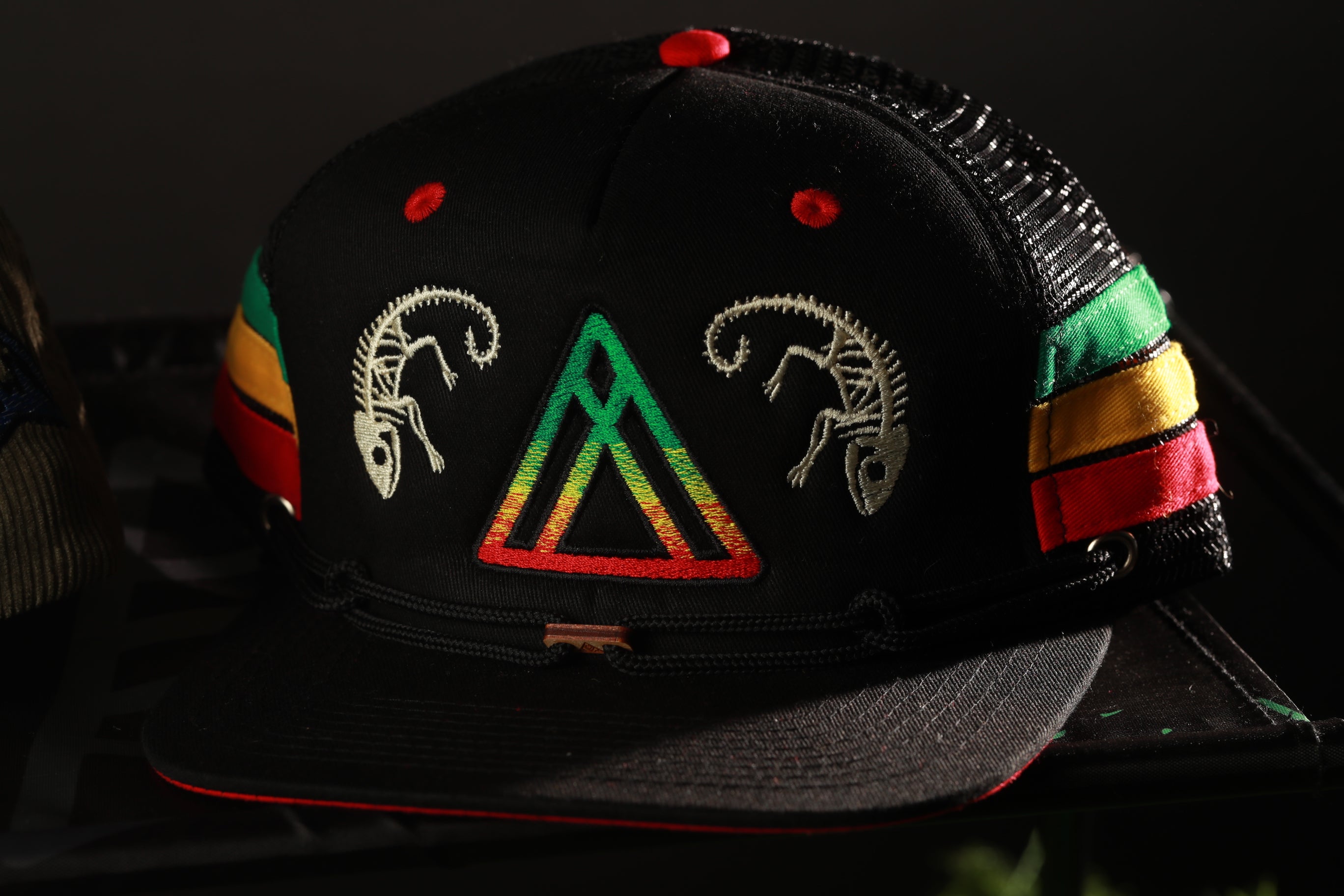 A black baseball cap with colorful designs and patterns, including a triangle and two stylized animal figures.