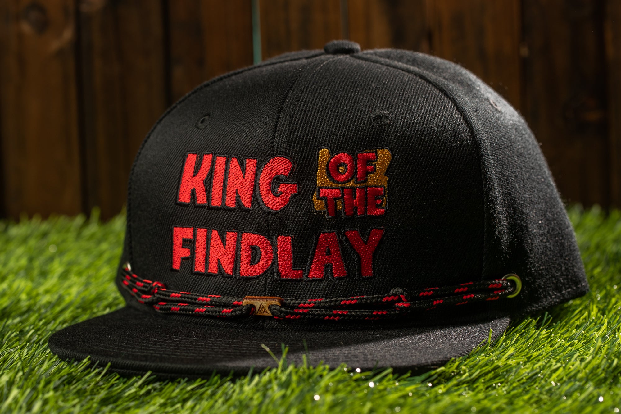 A black baseball cap with red text on it, sitting on a grassy surface.