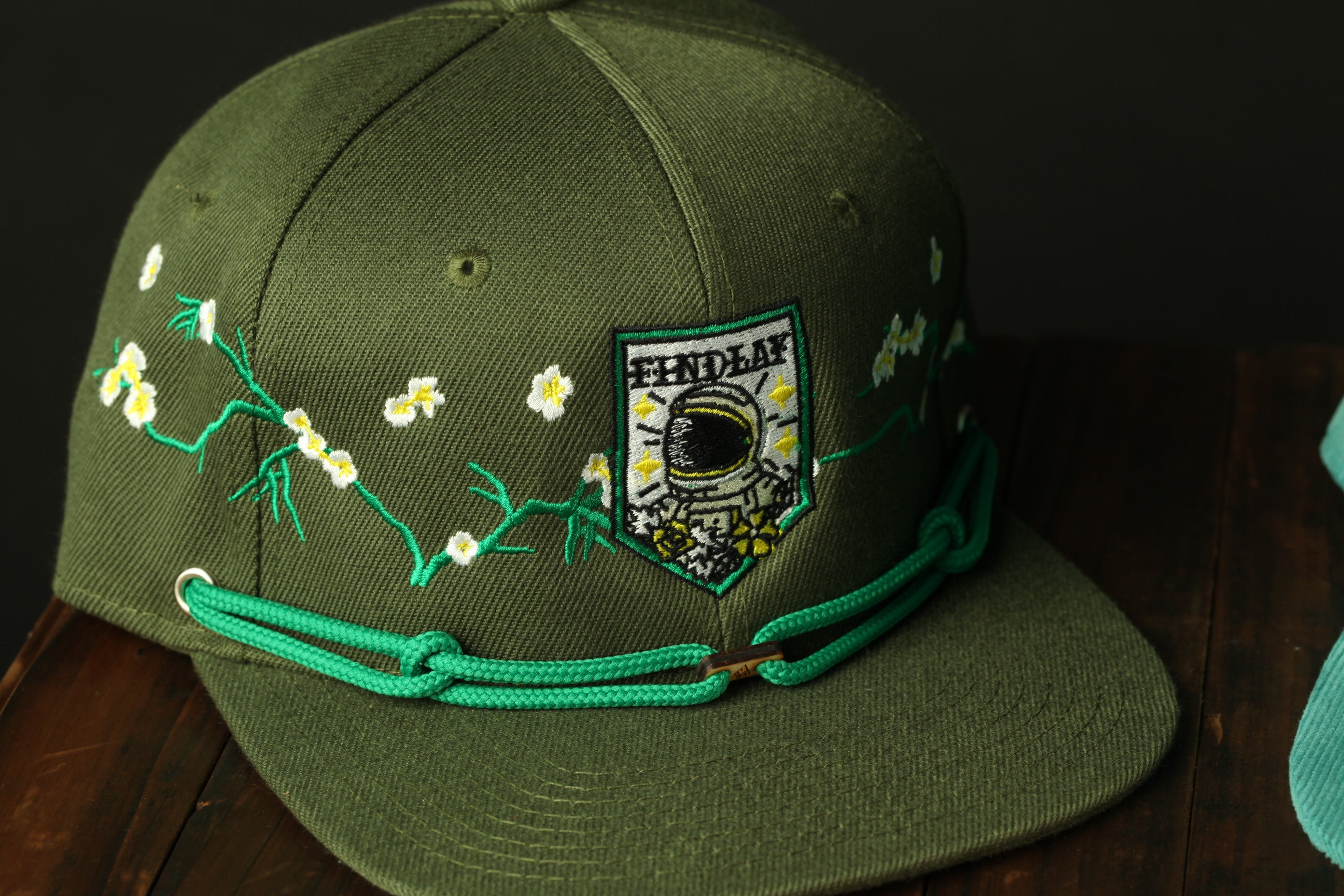 A green baseball cap with a floral design and a patch featuring a person's face.