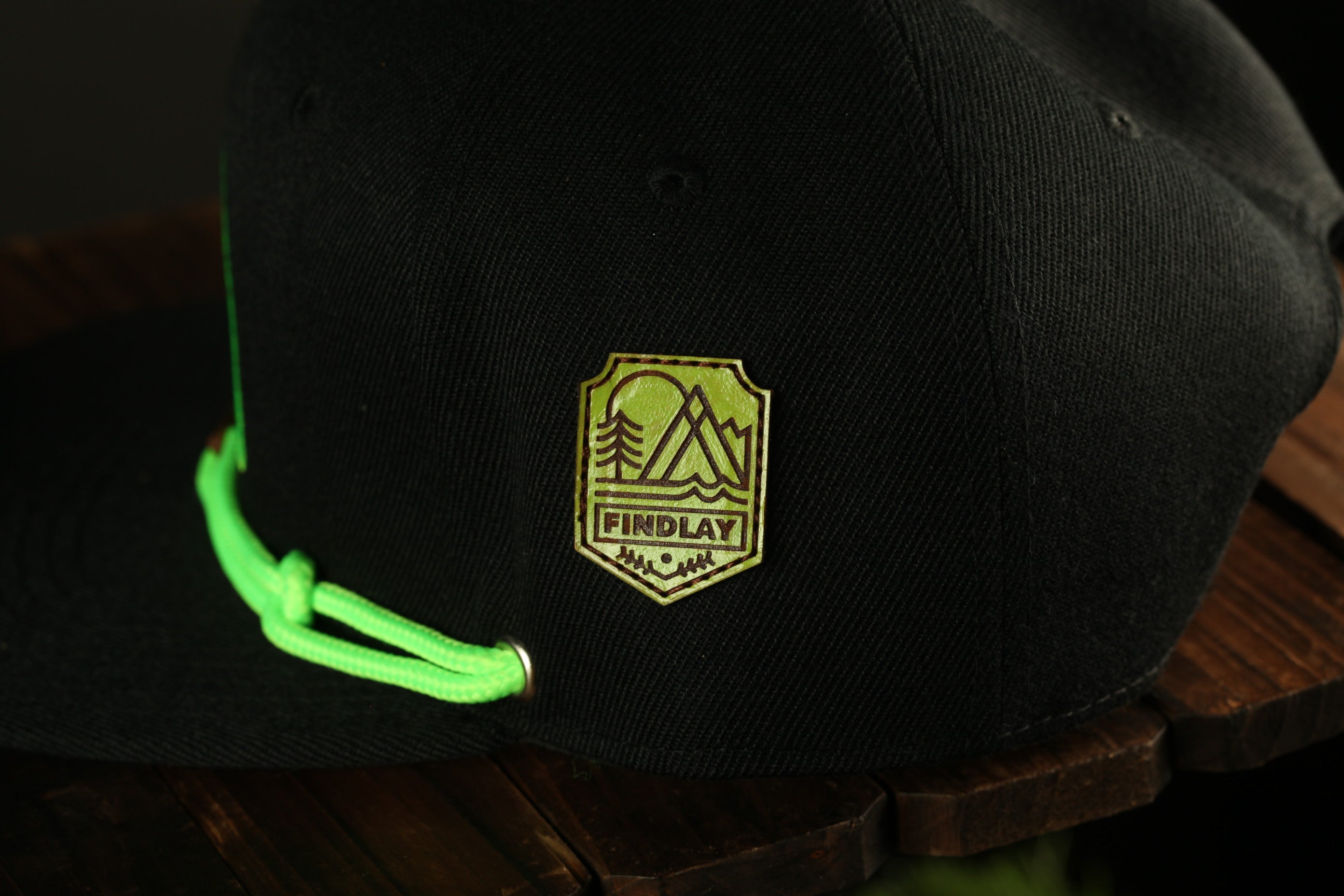 A black baseball cap with a green string attached, featuring a yellow and green logo on the front.