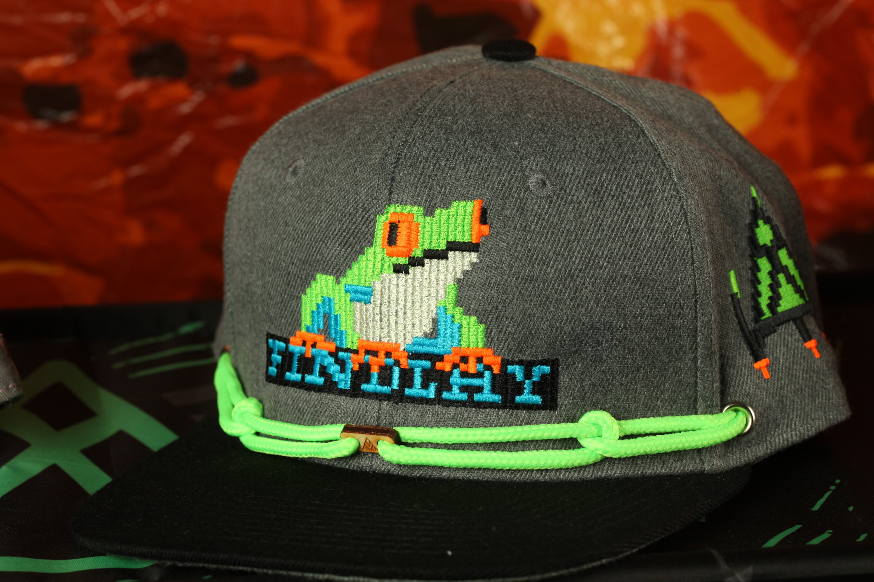 A gray baseball cap with a frog embroidered on it, featuring a neon green string around the brim.