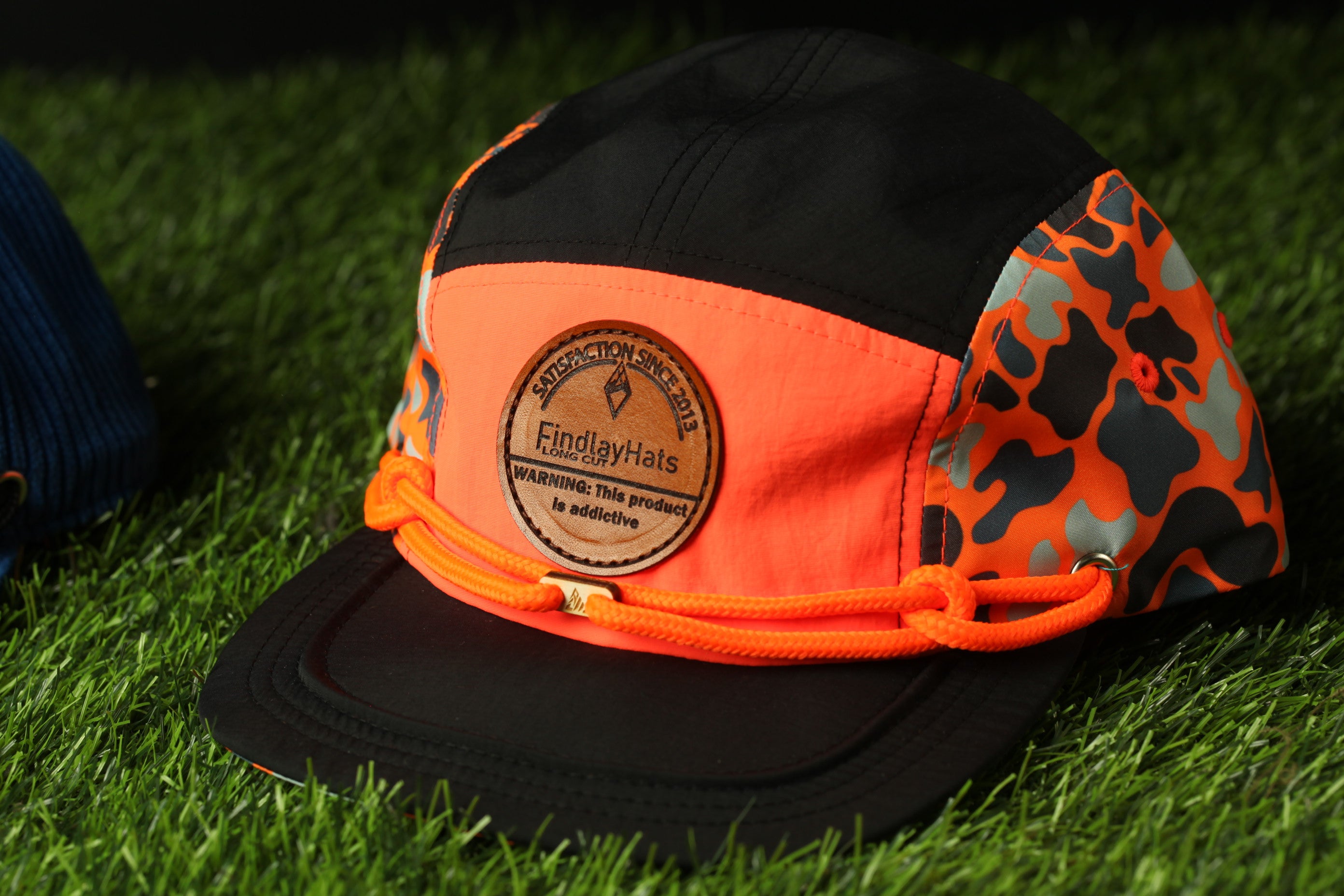 A black and orange baseball cap with a circular logo on the front, lying on a grassy surface.
