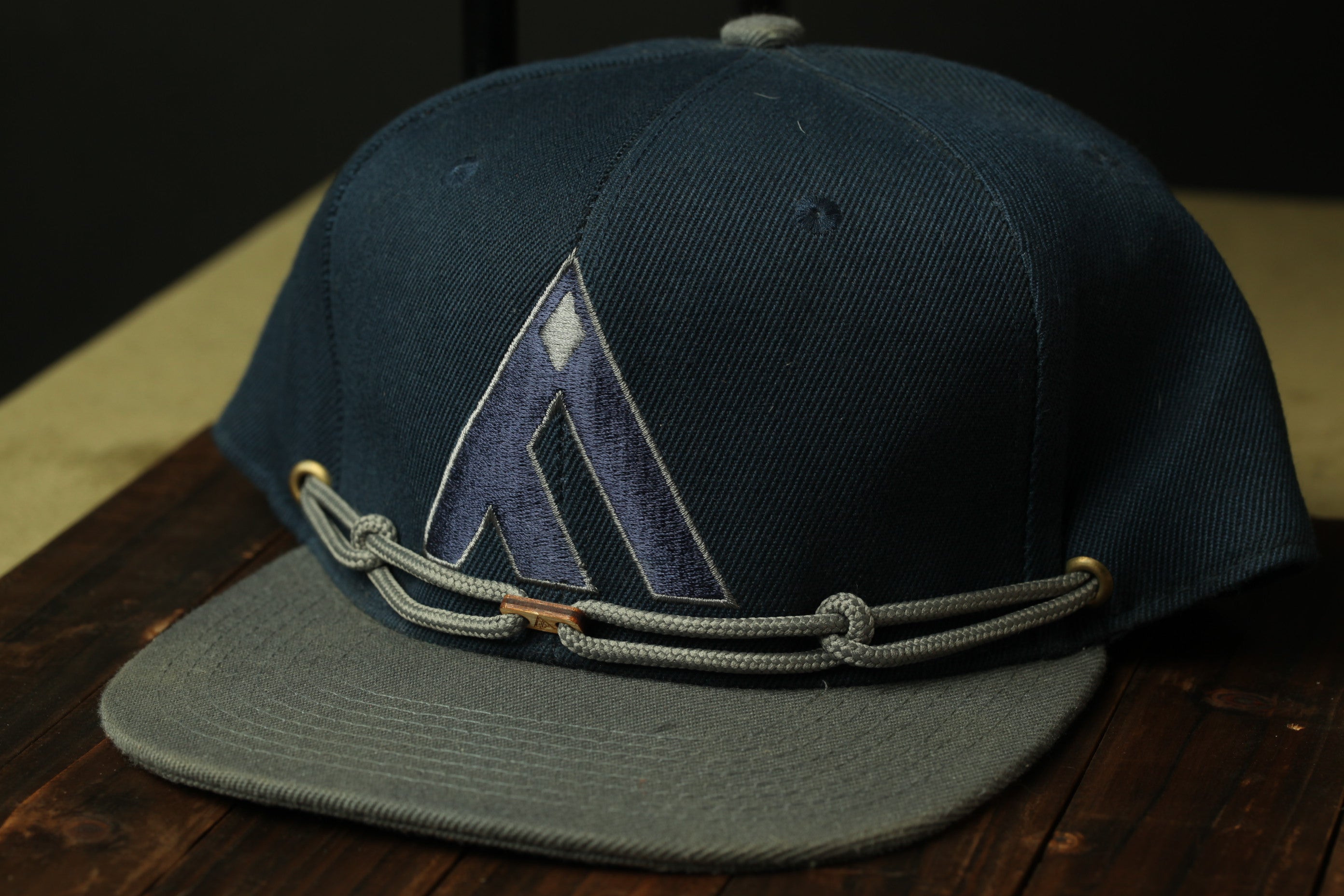 A dark blue baseball cap with a gray brim and a gray chain strap is displayed on a wooden surface.