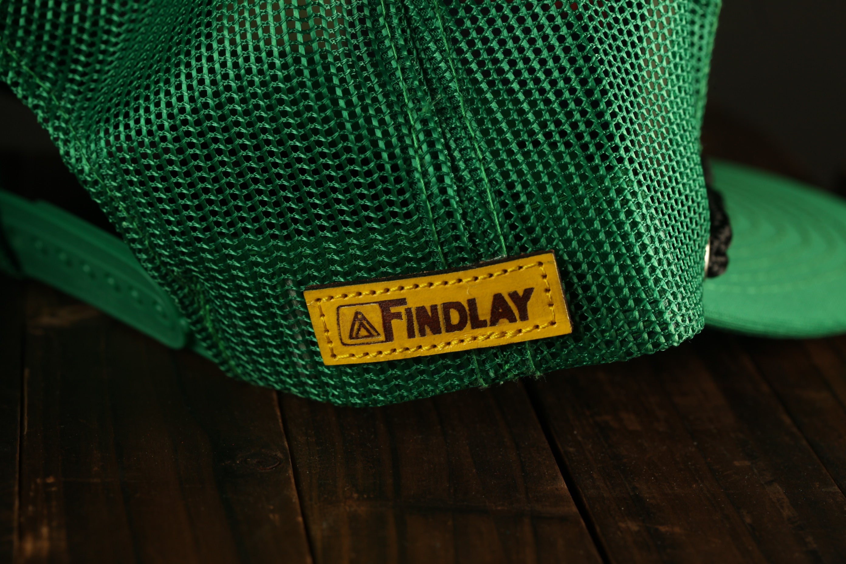 A close-up view of a green mesh baseball cap with a yellow "Findlay" label attached to it.