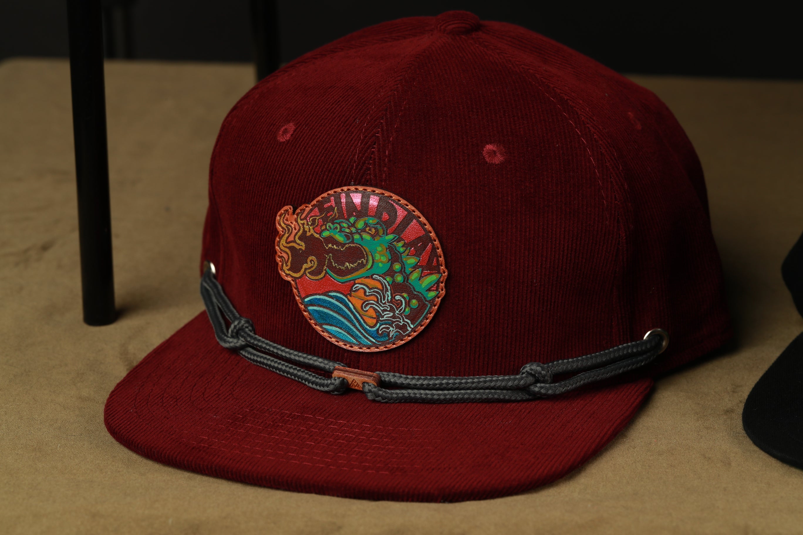 A burgundy baseball cap with a colorful dragon design on the front.