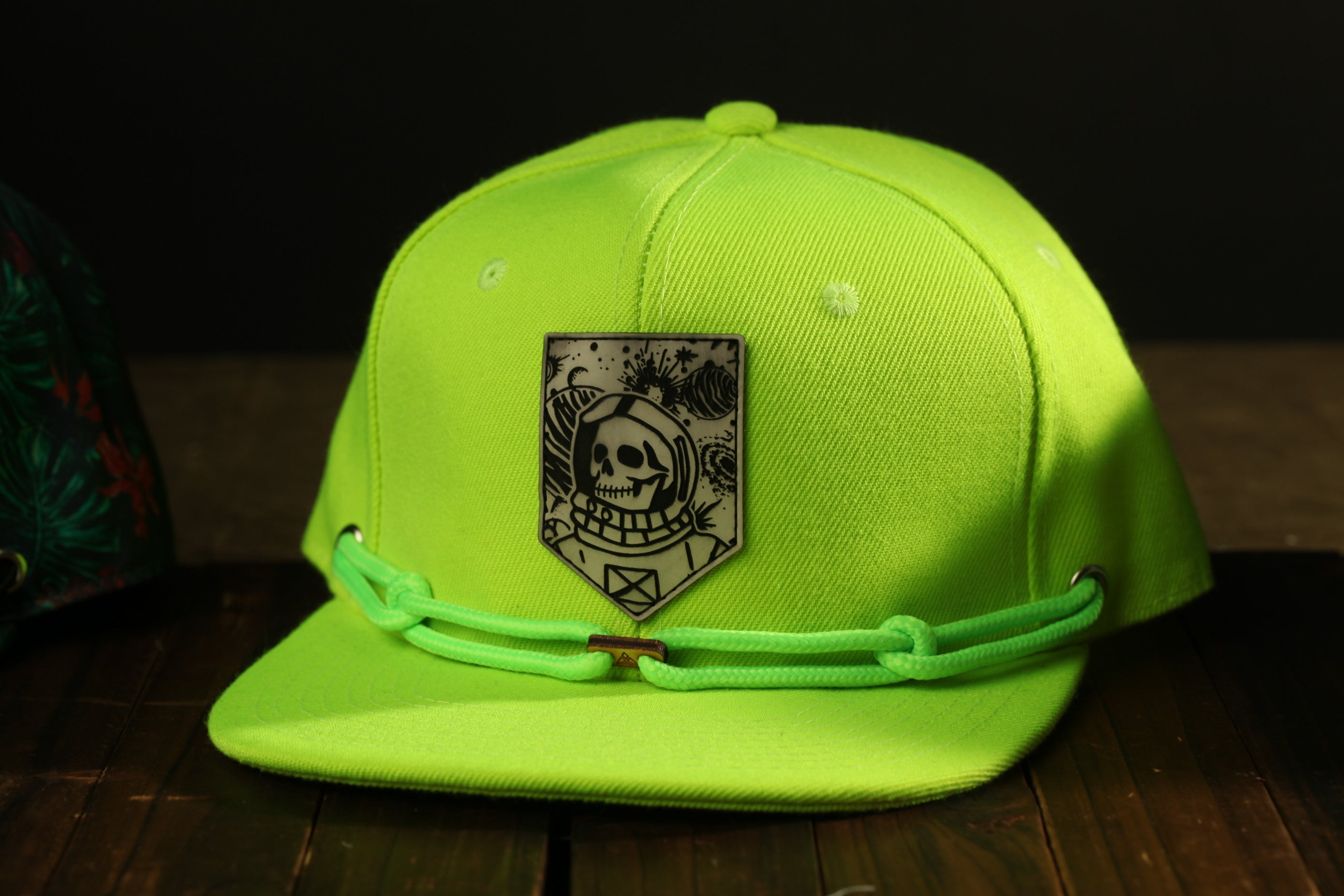 A bright green baseball cap with a skull and crossbones design on the front, sitting on a wooden surface.