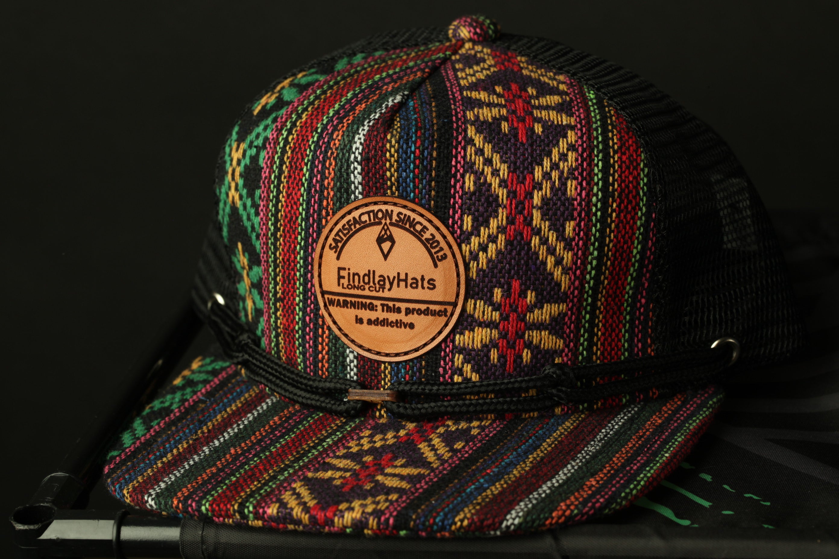 A colorful, patterned baseball cap with a leather patch on the front, featuring a warning label.