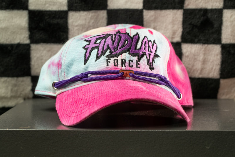 A pink and purple baseball cap with the text "FINDlay Force" printed on it, sitting on a black surface against a checkered background.