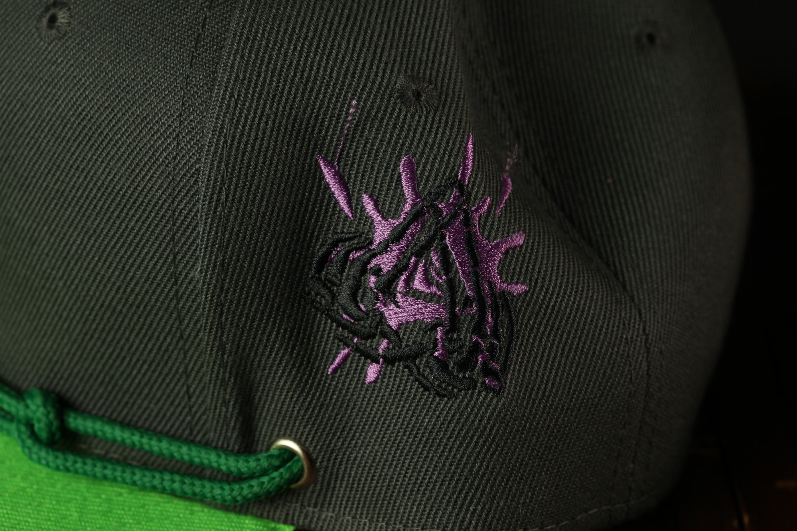 a close-up view of a black baseball cap with a purple embroidered design on the front.