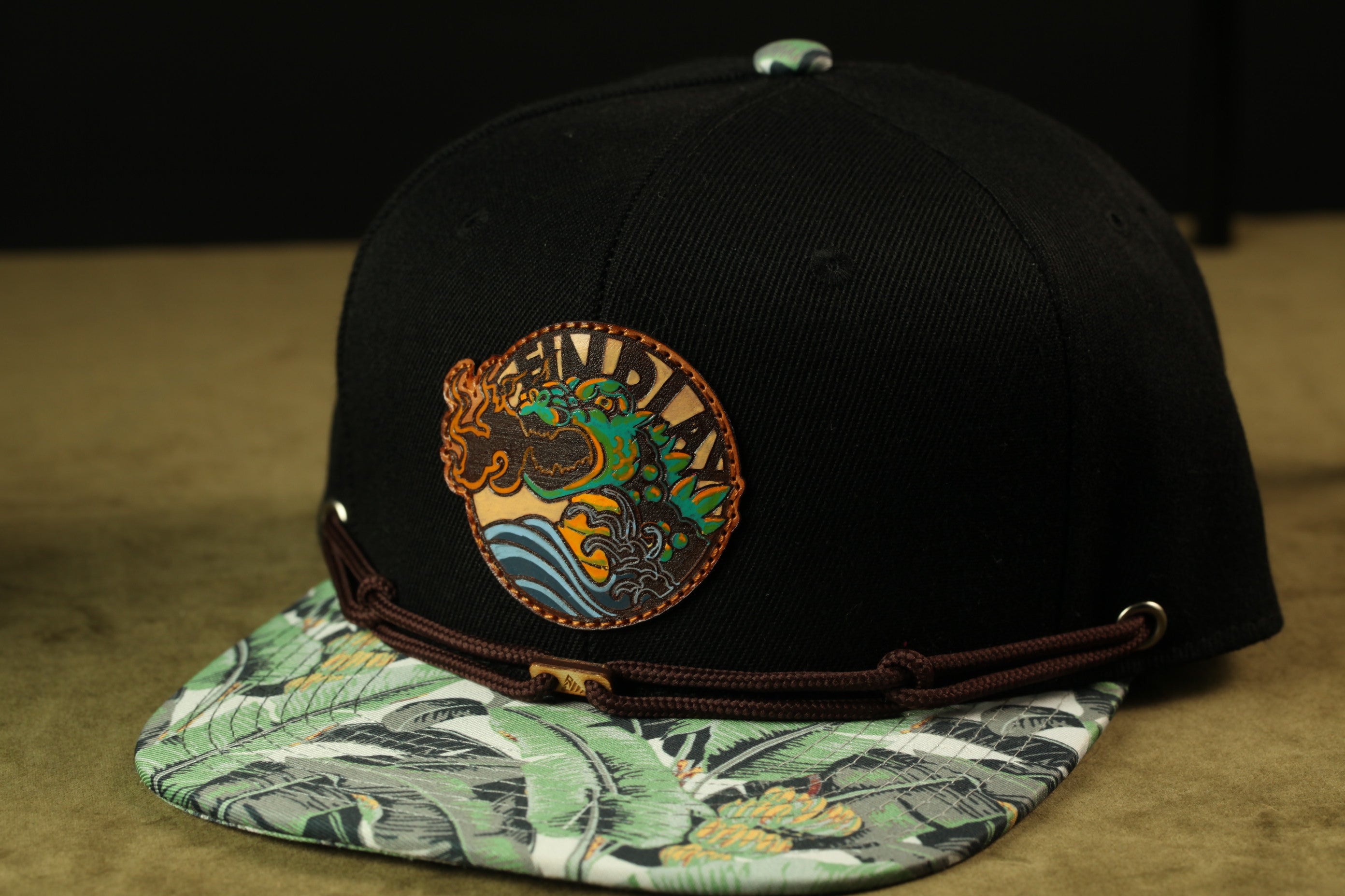 A black baseball cap with a tropical print pattern and a circular patch on the front.