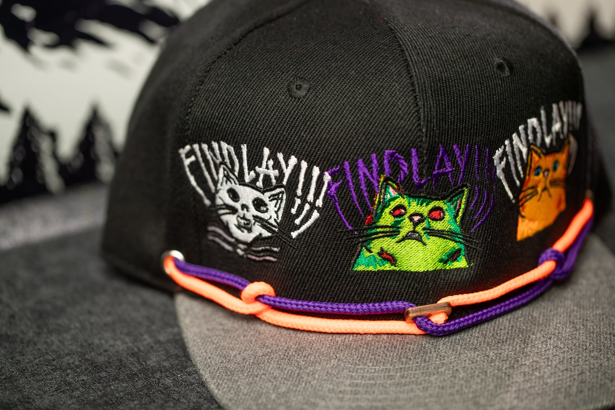 A black baseball cap with colorful cat designs and text on it.