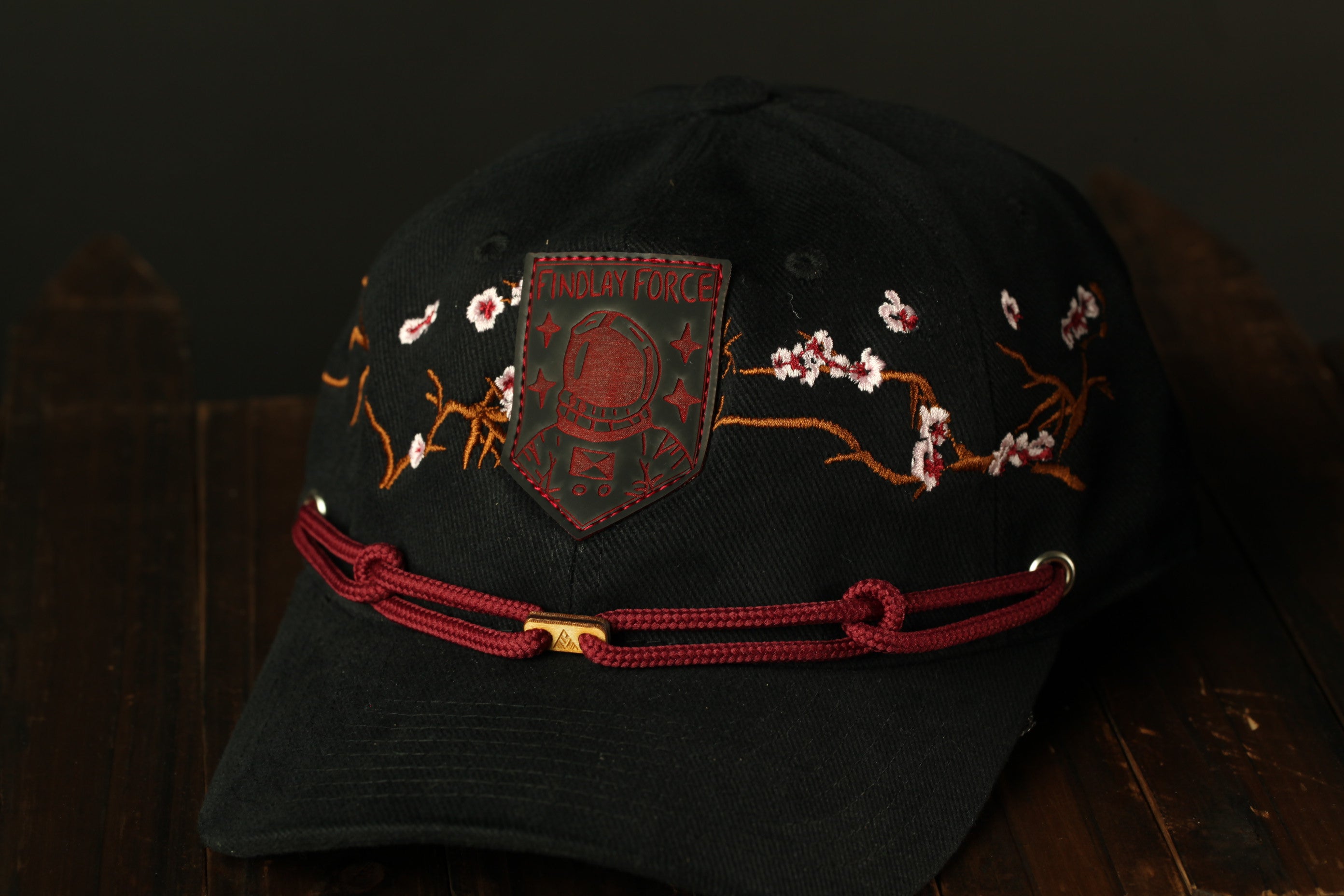 A black baseball cap with a red and gold embroidered design and a red band around the brim.