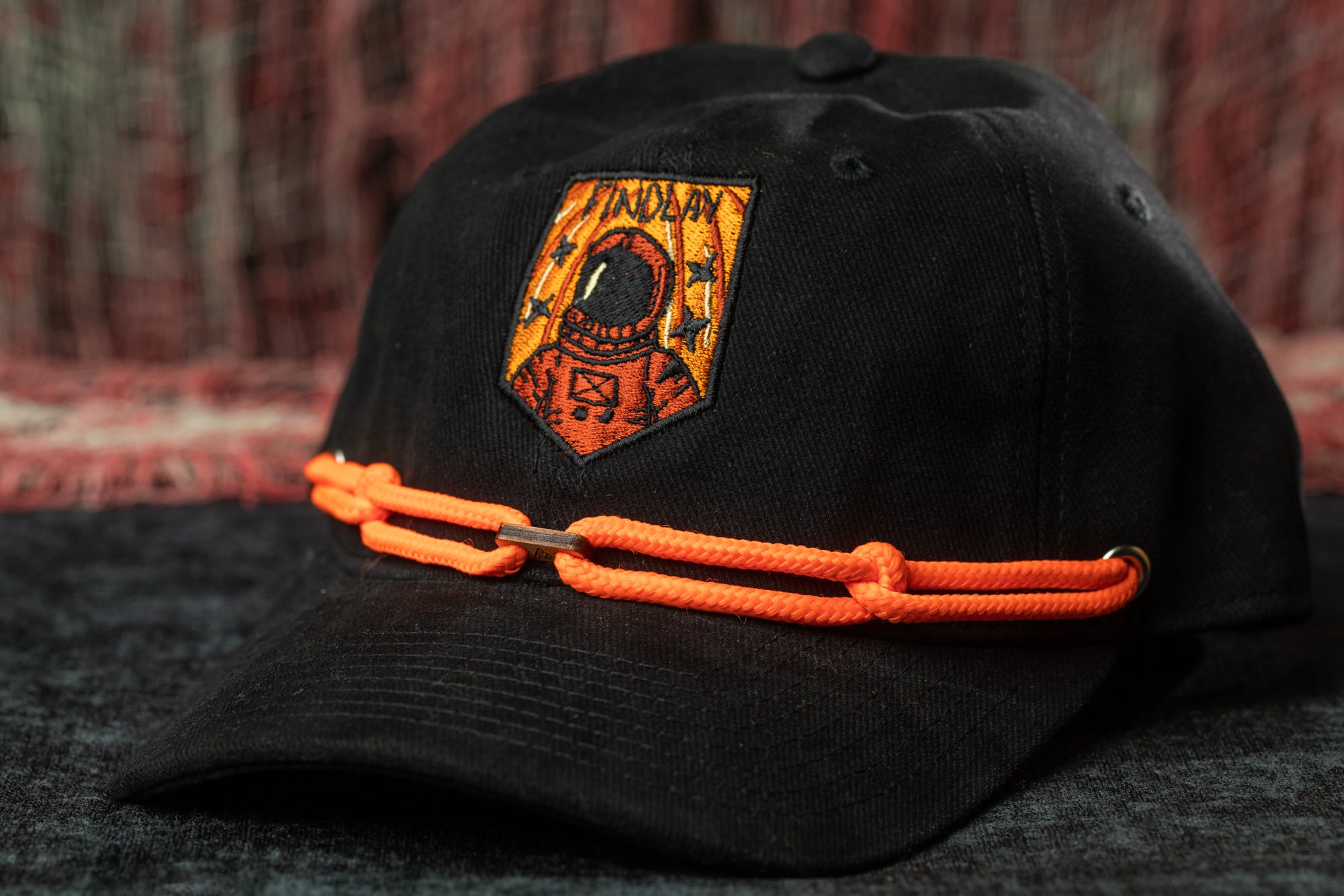 A black baseball cap with an orange chain and an embroidered patch featuring an astronaut.