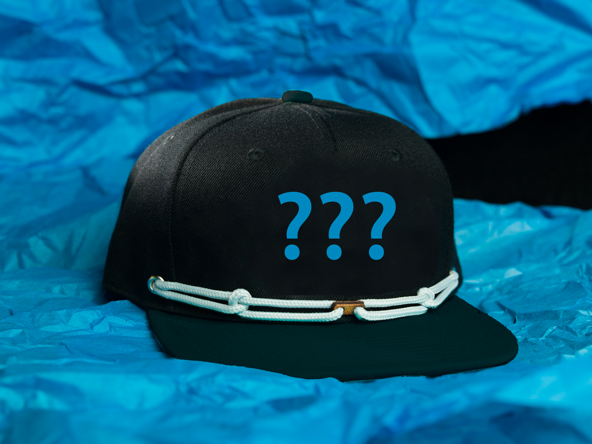 A black baseball cap with a white rope and three blue question marks printed on it, placed on a blue background.